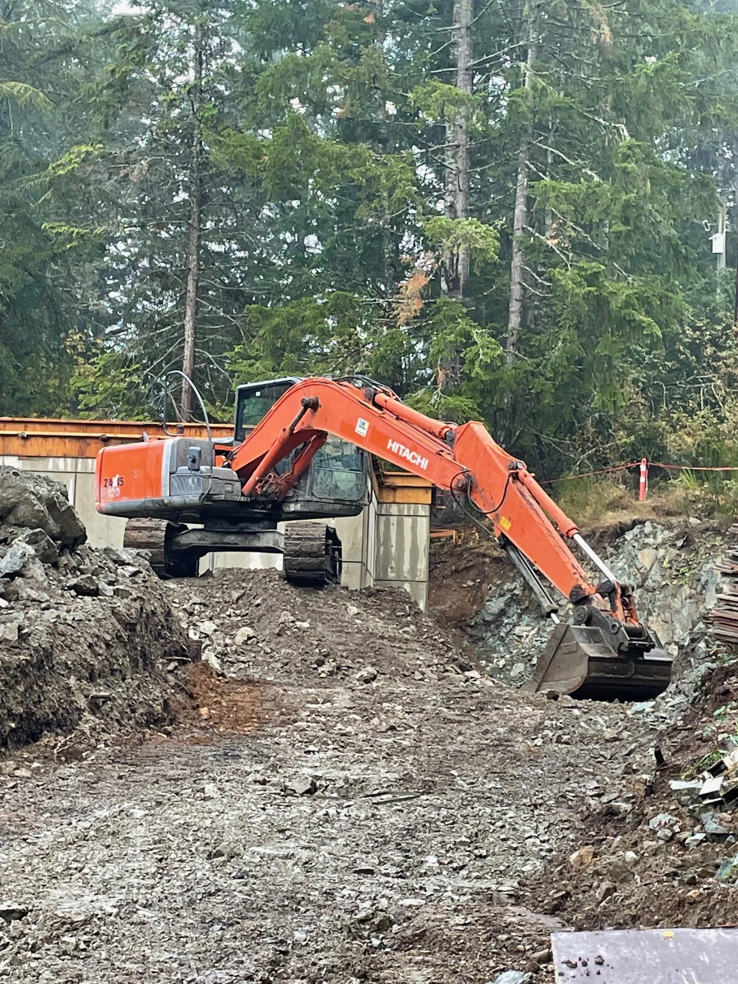 An orange Hitachi excavator working on a construction site surrounded by trees, dirt, and rocks.