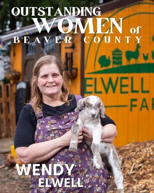 Wendy Elwell holding a puppy in front of a barn with a sign that reads "ELWELL FARM."