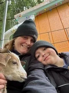 A woman and a boy smiling with a dog outside.