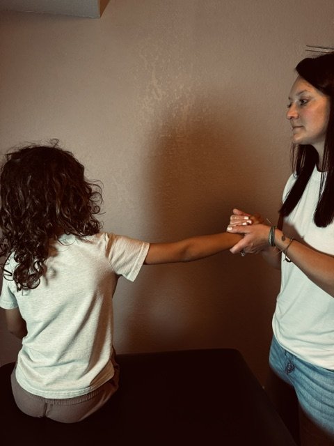 Nicole Amisone gently unwinding a child's arm during a craniosacral and fascial therapy session at Rapha Fascial Therapy in Rapid City, South Dakota.