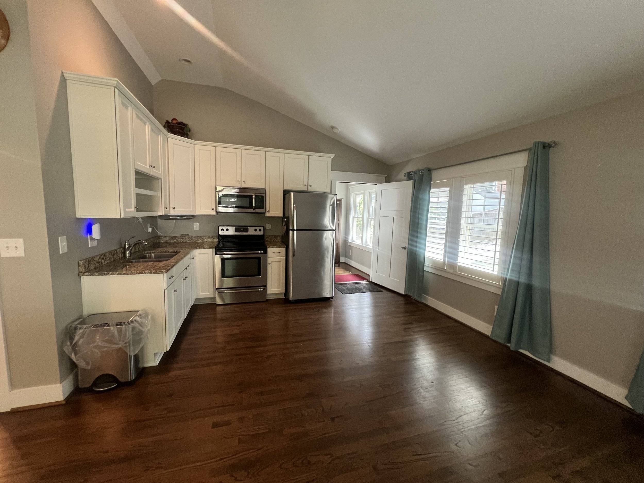 A kitchen with white cabinets, a stainless steel refrigerator, a stove, and a window with blue curtains.