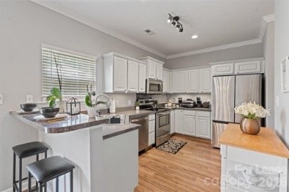 Modern kitchen with white cabinets, stainless steel appliances, and a breakfast bar with two stools.