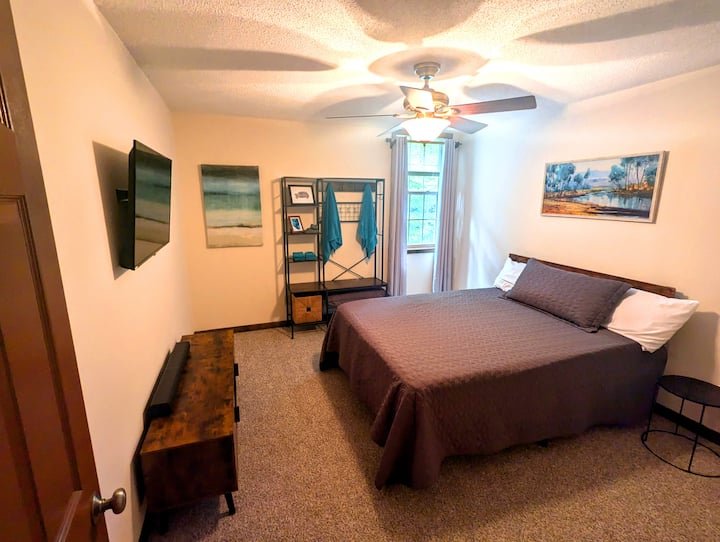 A cozy bedroom with a bed, side table, wall-mounted TV, closet organizer, and artwork on the walls.