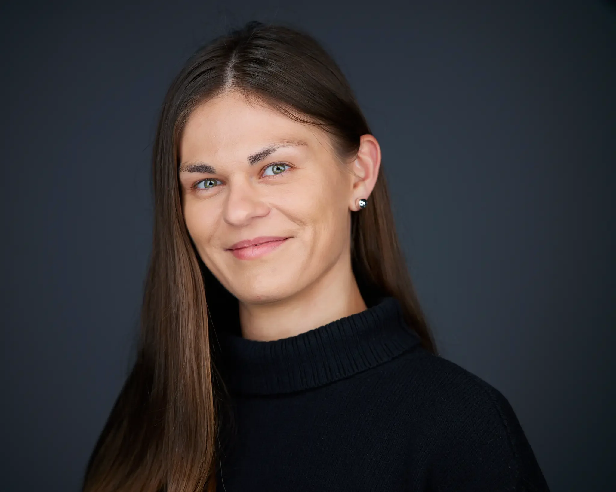 Portrait of a woman with long brown hair, wearing a black turtleneck, smiling softly, against a dark background.