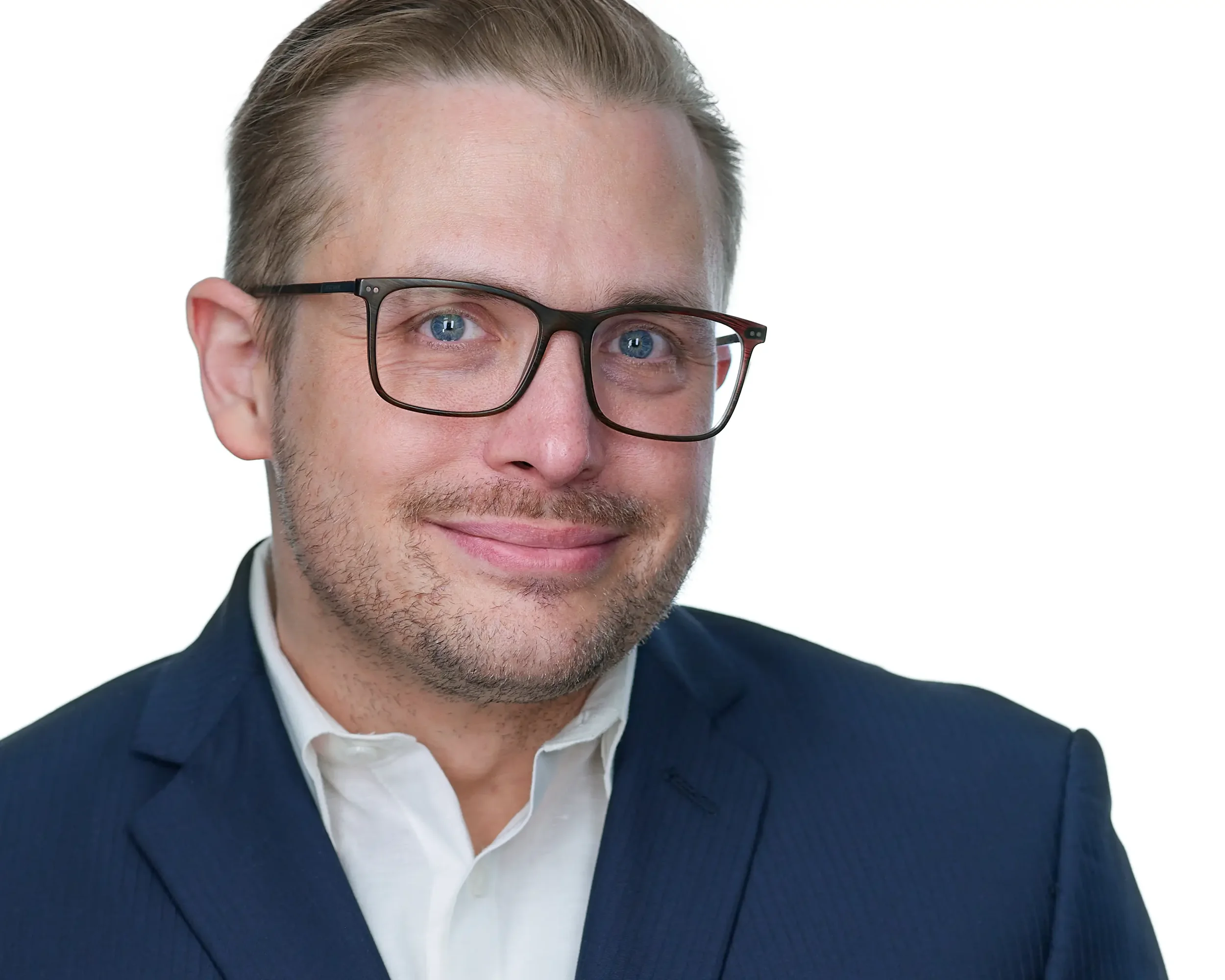 A professional man with light skin, short blond hair, wearing black glasses, a navy blue suit, and a white shirt, smiling against a plain white background.