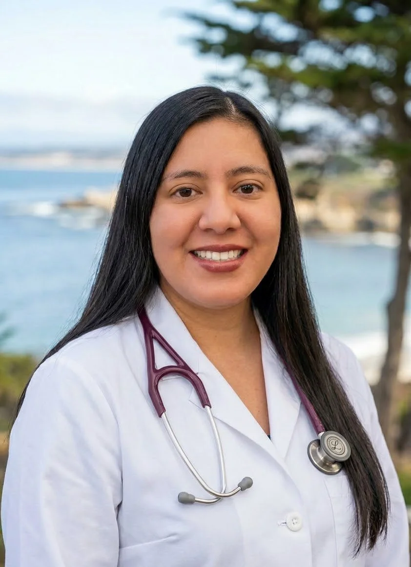 A female healthcare professional with long black hair, wearing a white lab coat with a stethoscope around her neck, standing outdoors near water with trees and buildings in the background.