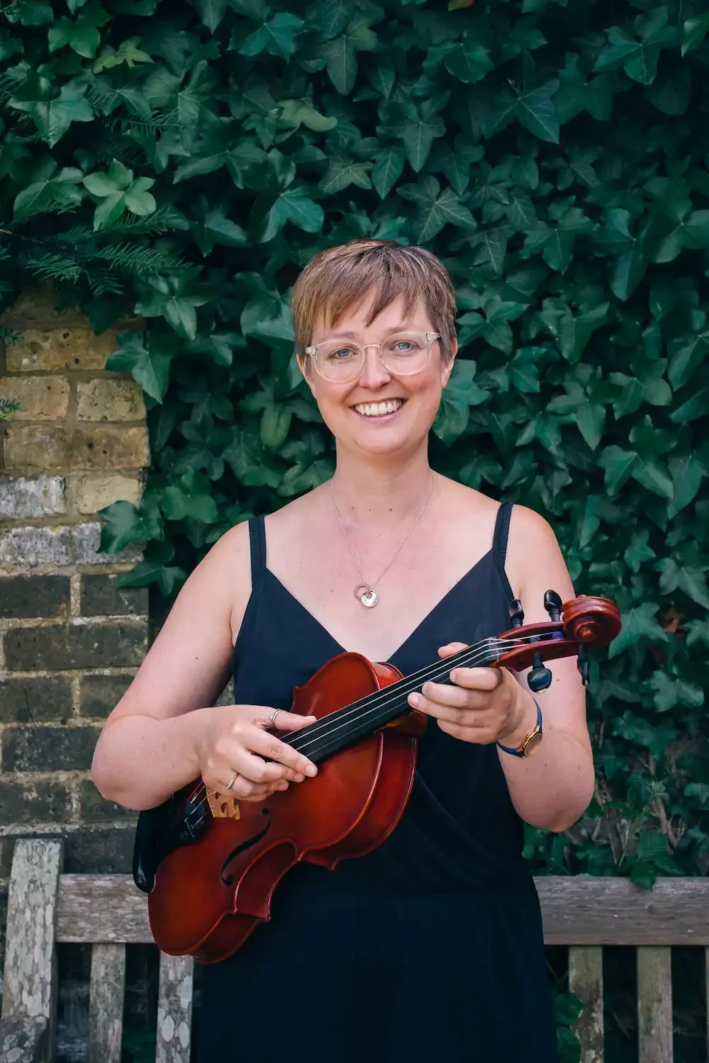 Violist Anna posing with her instrument in front of a bench and greenery