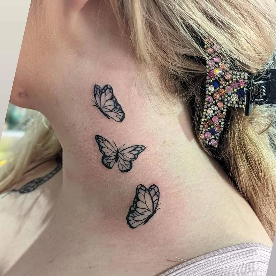Tattoo of three black butterfly outlines on a person's neck, with one near the ear and two downward.