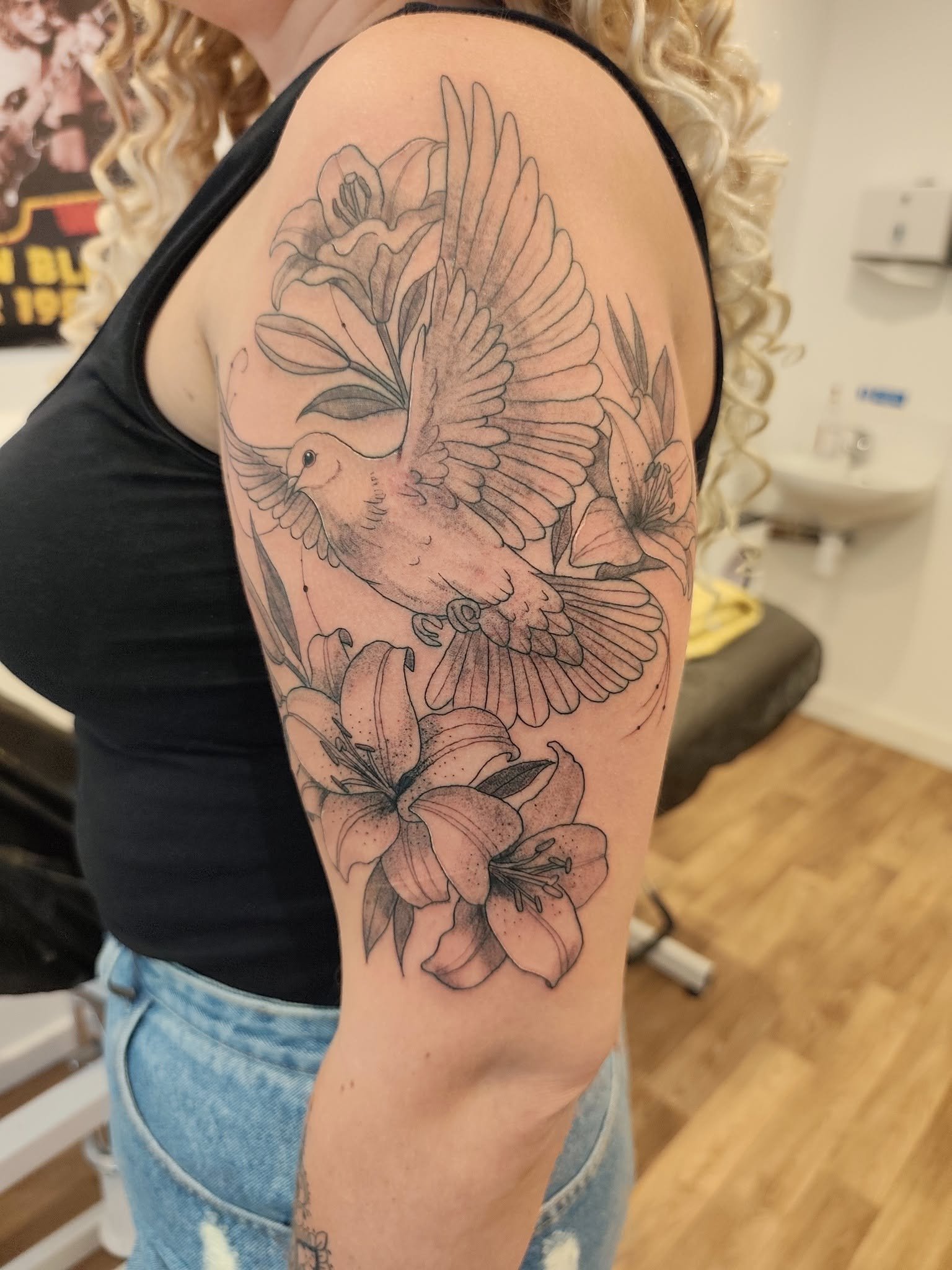 Tattoo of a bird flying among flowers on a person's upper arm.