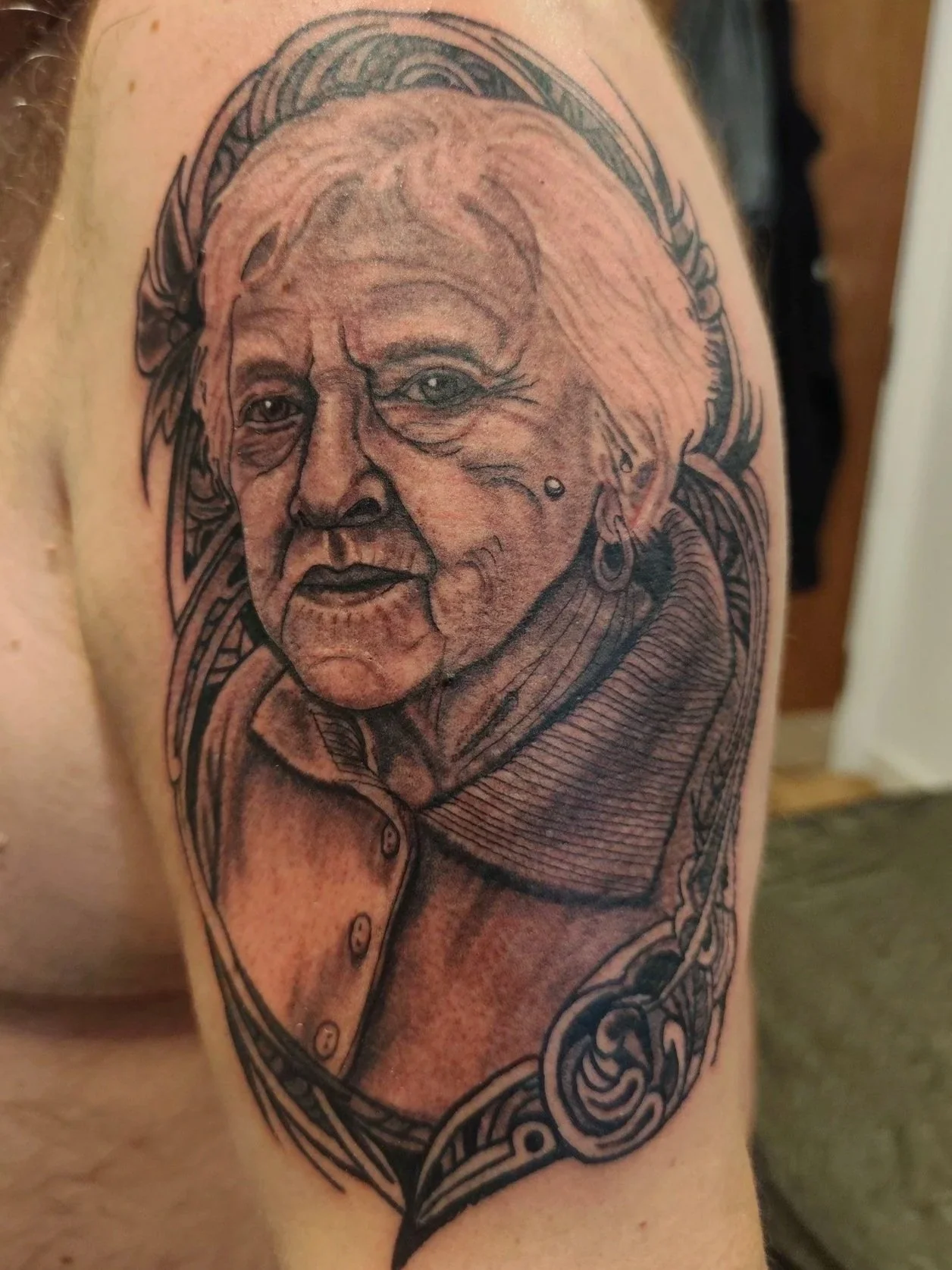 Tattoo portrait of a  woman with earrings, detailed facial features, and wearing a collared shirt, framed with ornamental line work.