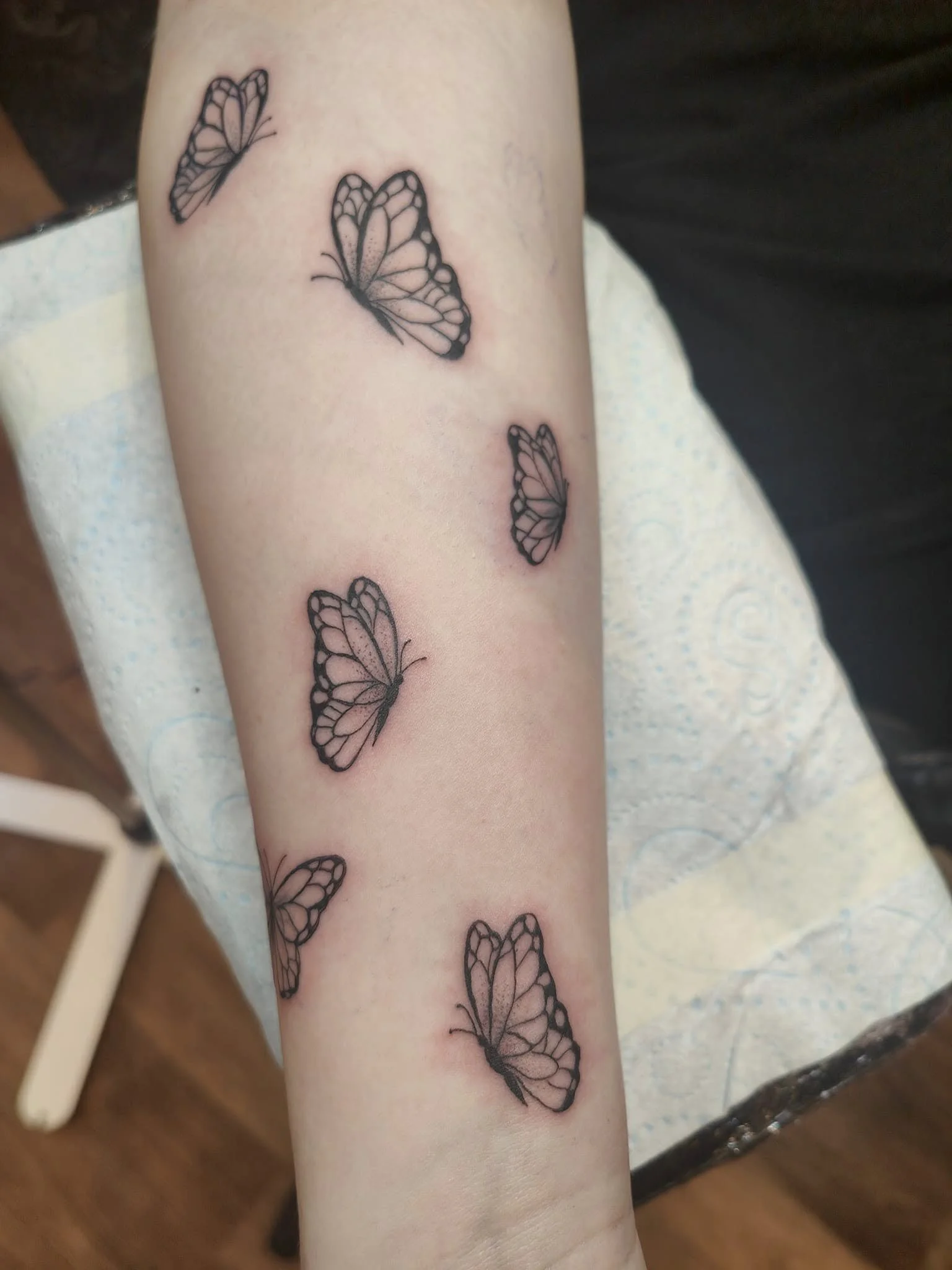 Tattoo of several monarch butterflies on a person's forearm with black outlines and pink shading.