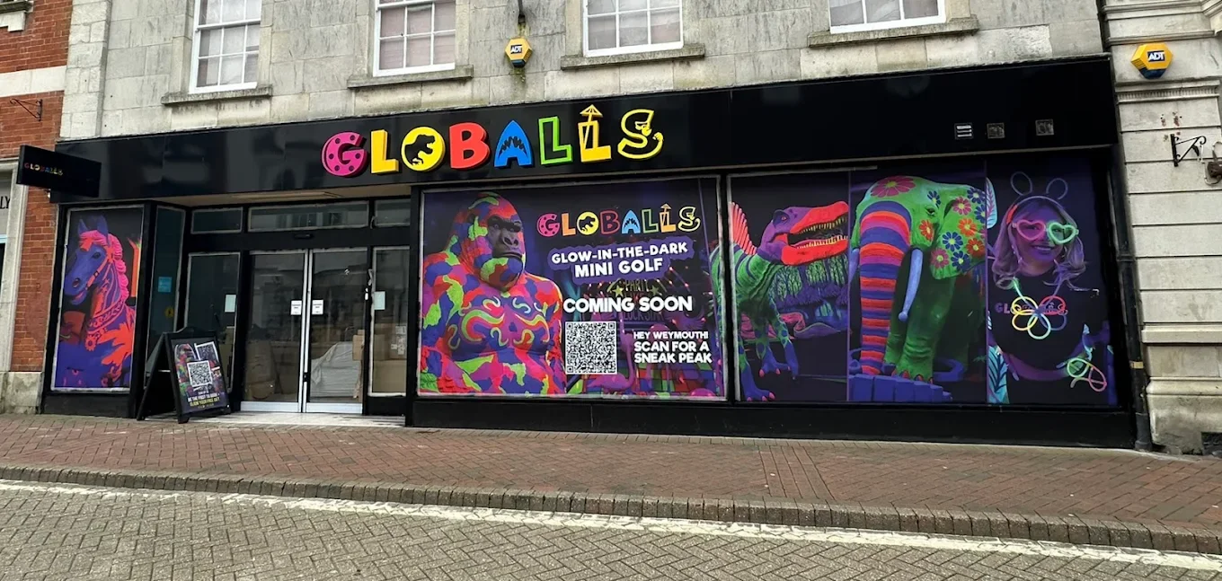 Storefront with colorful, neon-style drawings of animals and a girl with sunglasses and neon hair accessories. Sign promotes a glow-in-the-dark mini golf attraction coming soon.