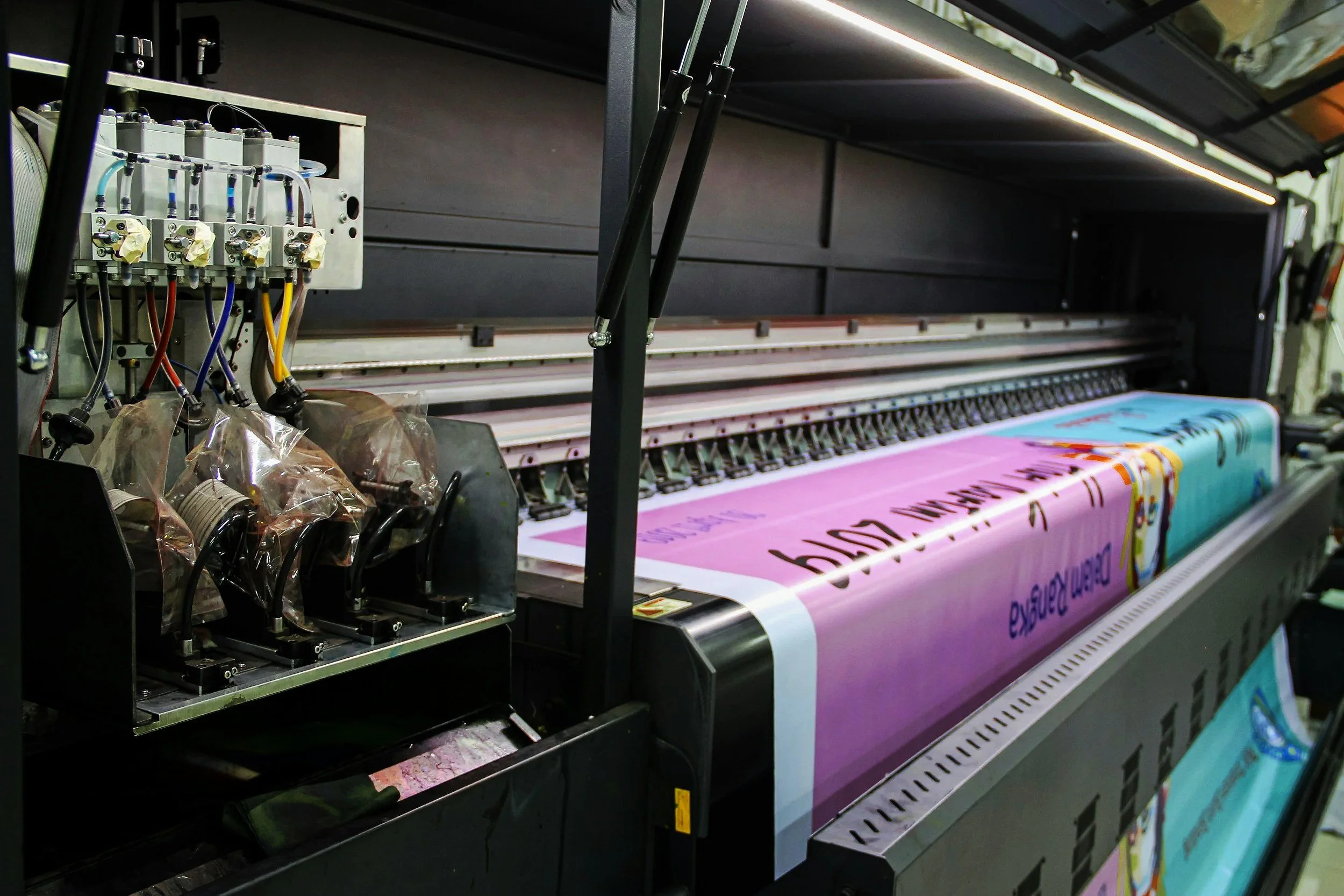 Large digital printer printing colorful banners with text and graphics.