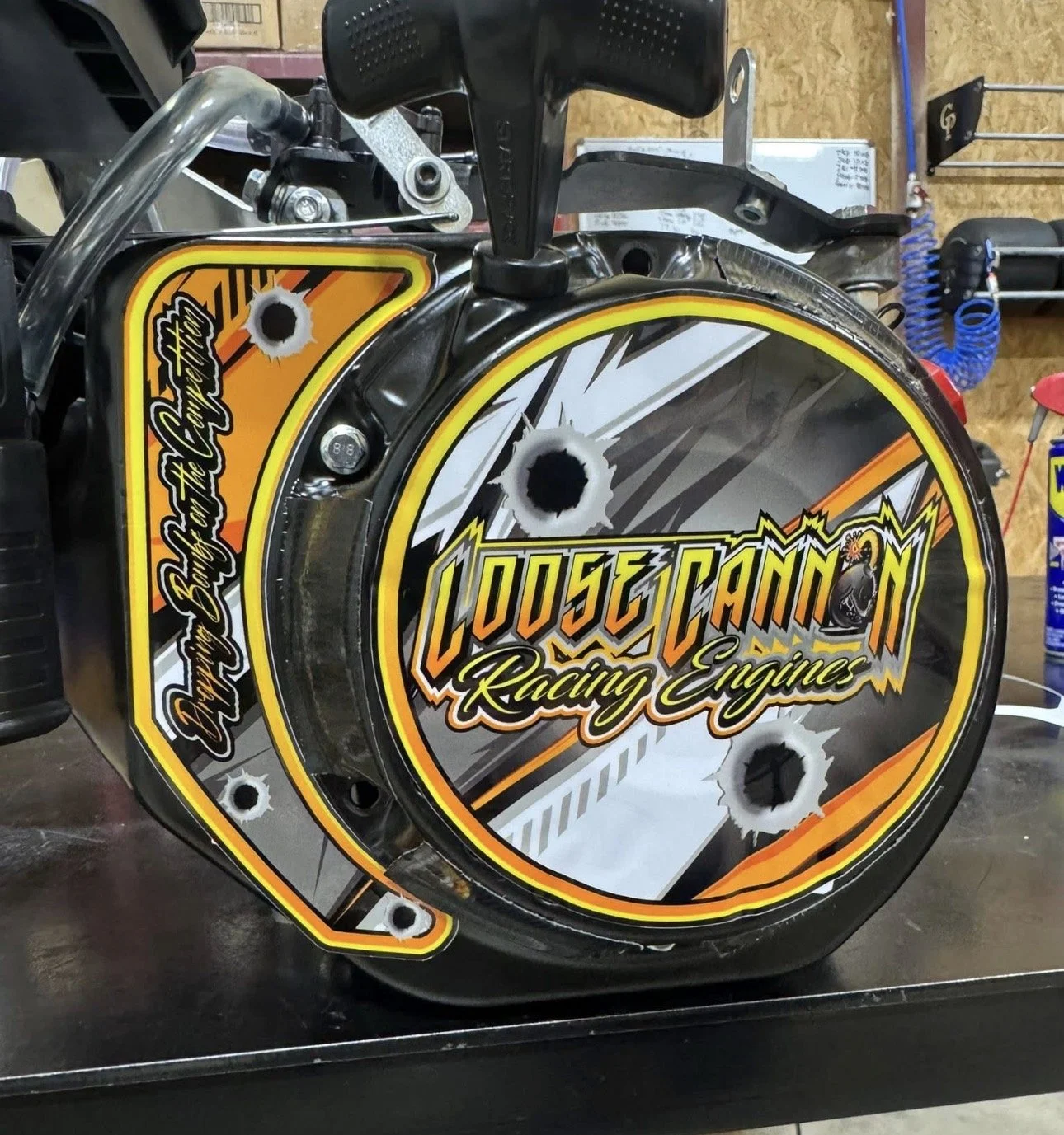 A racing engine cover with a graphic design and bullet holes.