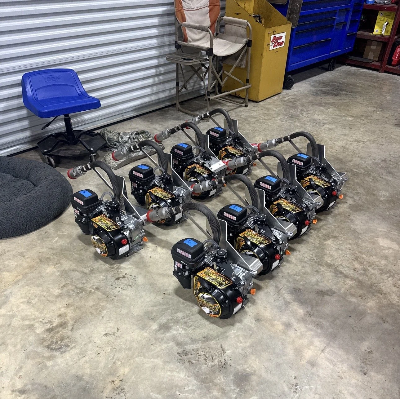 Six mini high-performance engines lined up on a concrete floor in a workshop space.