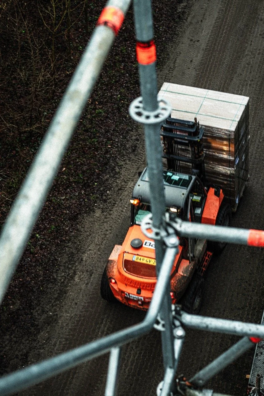 Een heftruck die pallets met materialen vervoert, gezien vanaf een hoge toren of bouwsteiger.