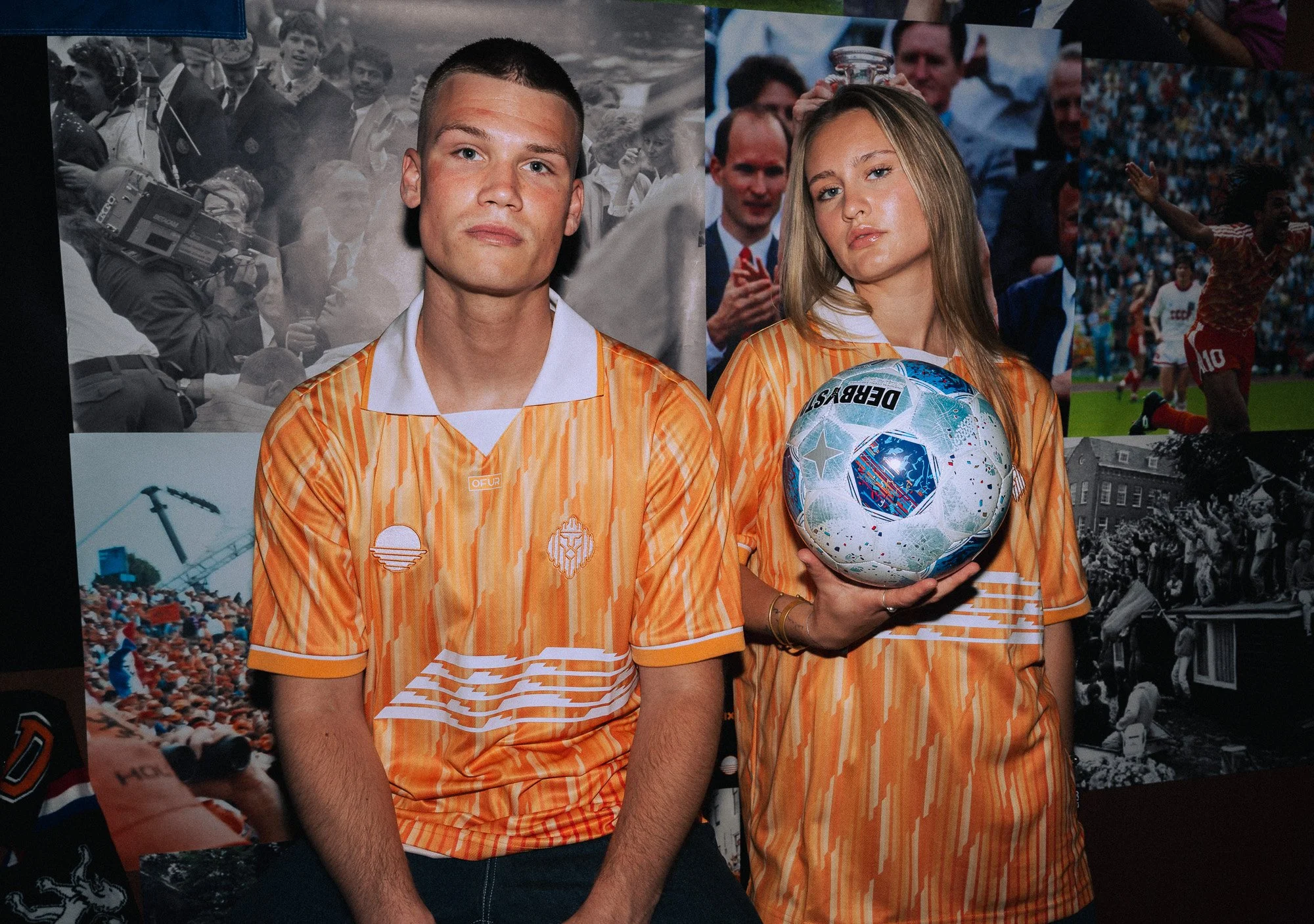 Twee jonge mensen in oranje sportshirts, een man en een vrouw, op een sportevenement. De vrouw houdt een voetbal vast en staat naast de man. Op de achtergrond zijn foto's en een crowd te zien.