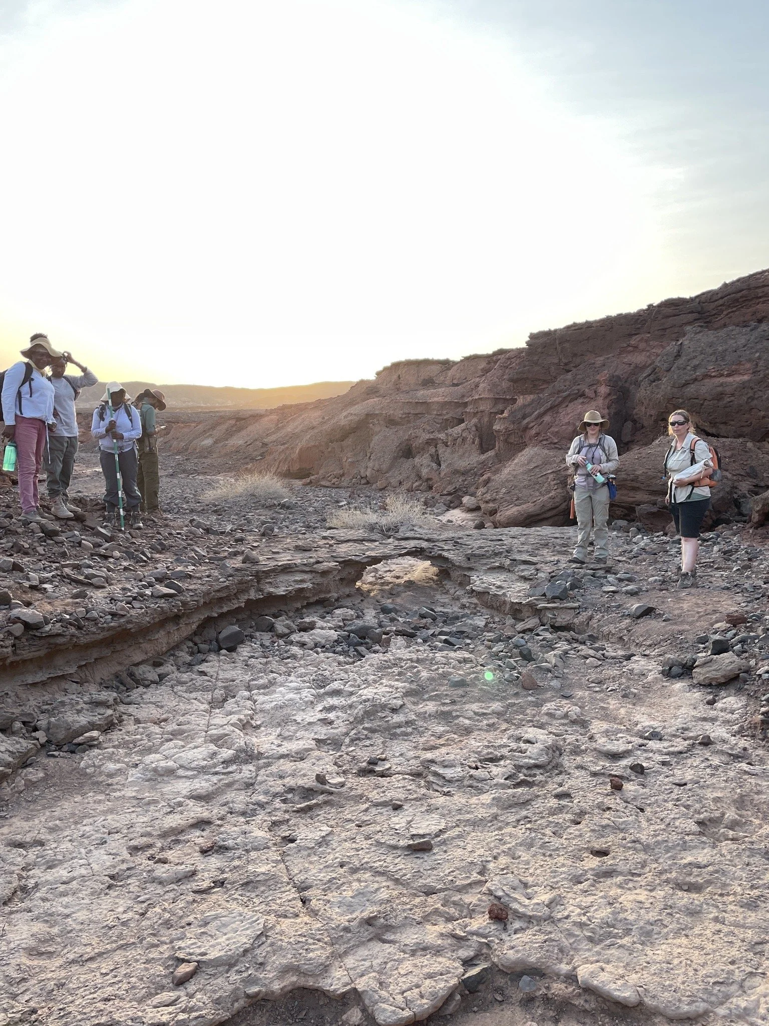 Group of hikers exploring a rugged, rocky desert landscape at sunset.