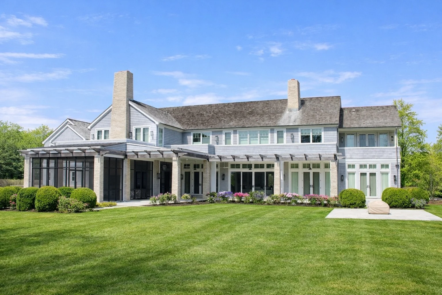 A large, modern house with a grey exterior, multiple windows, and a well-maintained green lawn with bushes and flowers in front