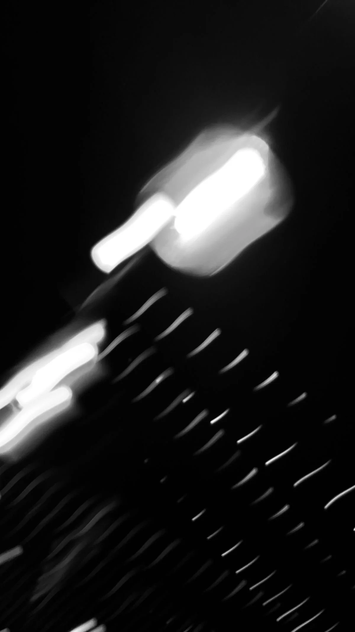 Blurred black and white image of illuminated objects on a dark background, possibly light fixtures or reflections.