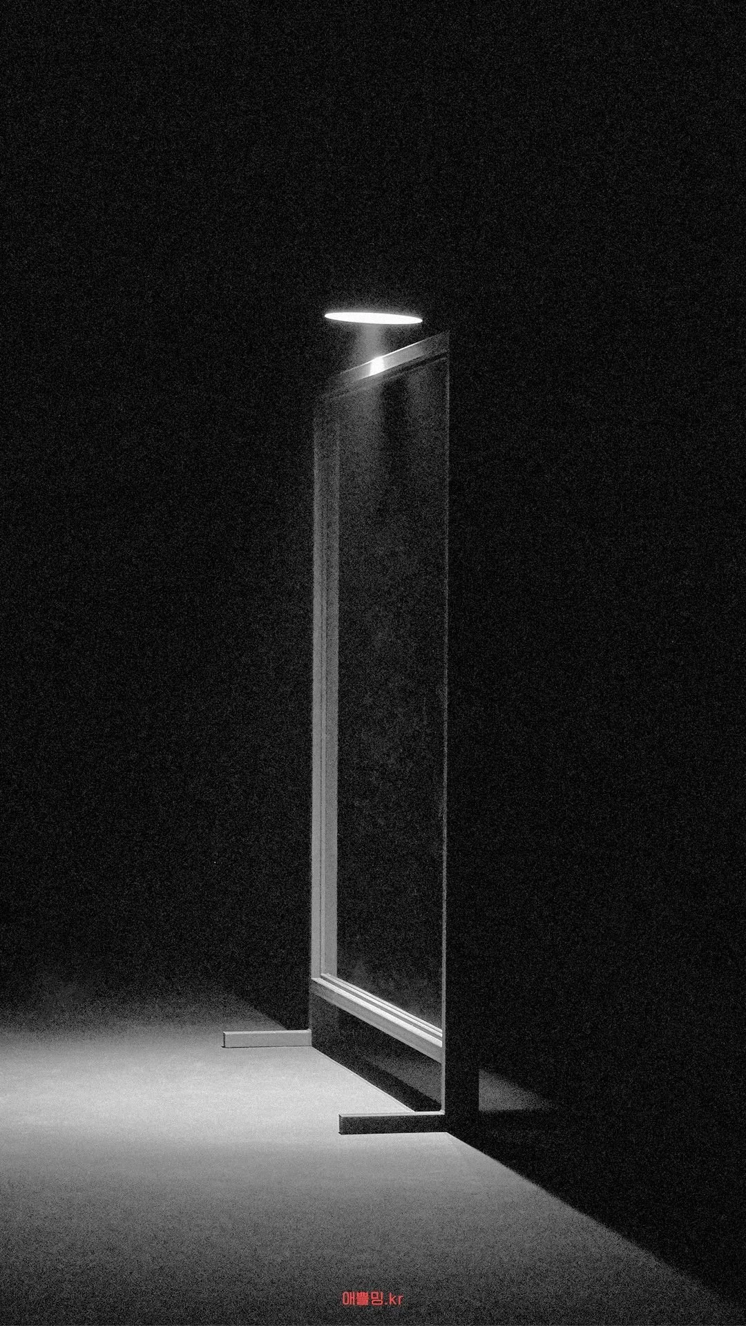 A minimalist, illuminated mirror standing on a dark surface with a single light above, casting a shadow on the floor.