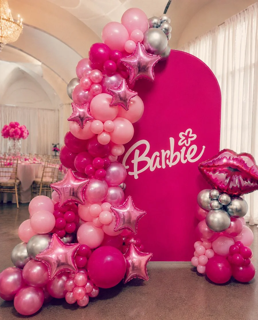 Pink and silver balloon arrangement with star-shaped and lips-shaped balloons in front of a pink backdrop with 'Barbie' written on it, set in an elegant event space.