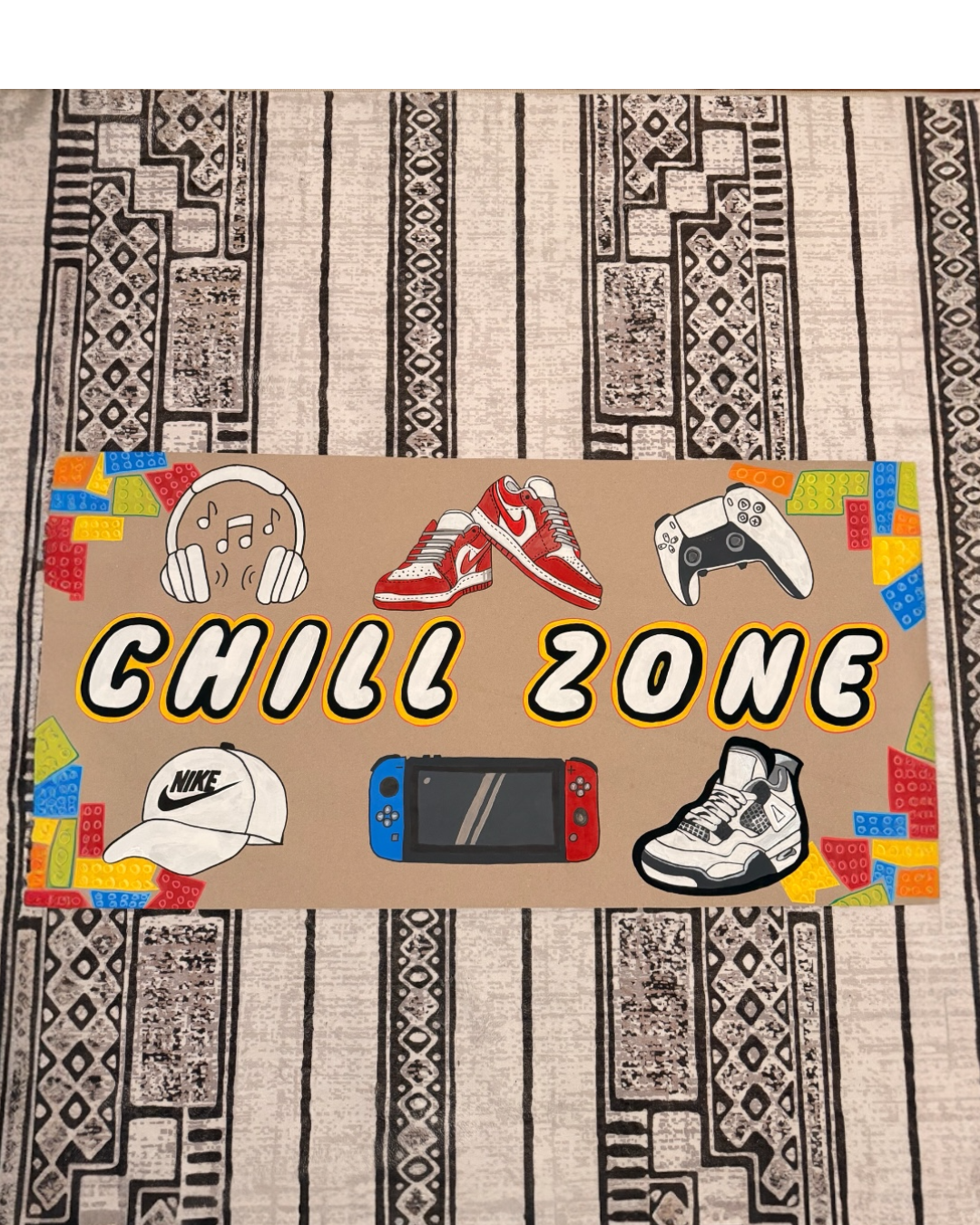 Colorful poster with illustrations of headphones, sneakers, a game controller, a cap, and a handheld gaming console, with the text 'Chill Zone' in the center, on a patterned floor.