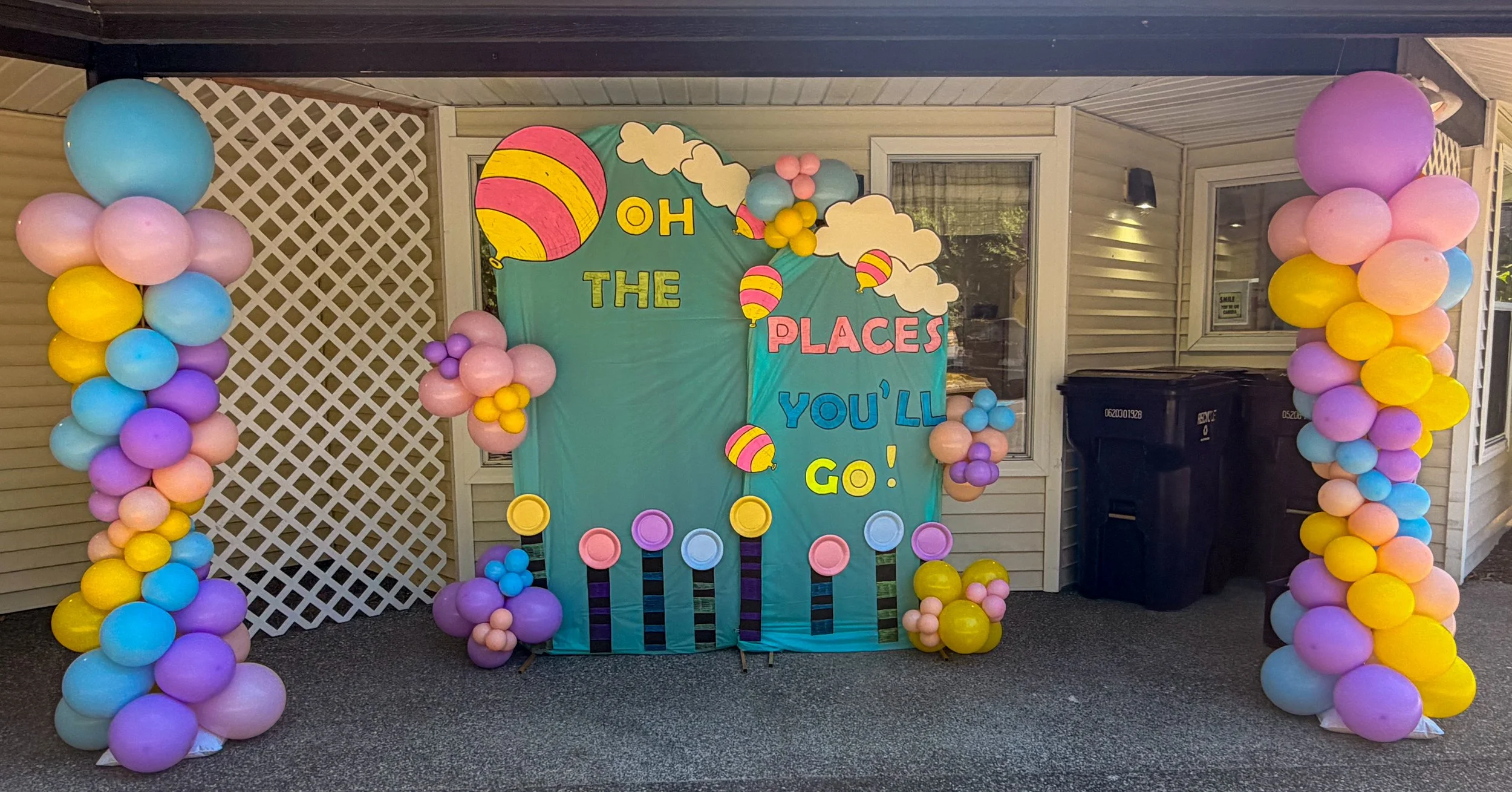 Colorful balloon arch and backdrop with a sign that says 'Oh The Places You'll Go!' for a celebration or party.