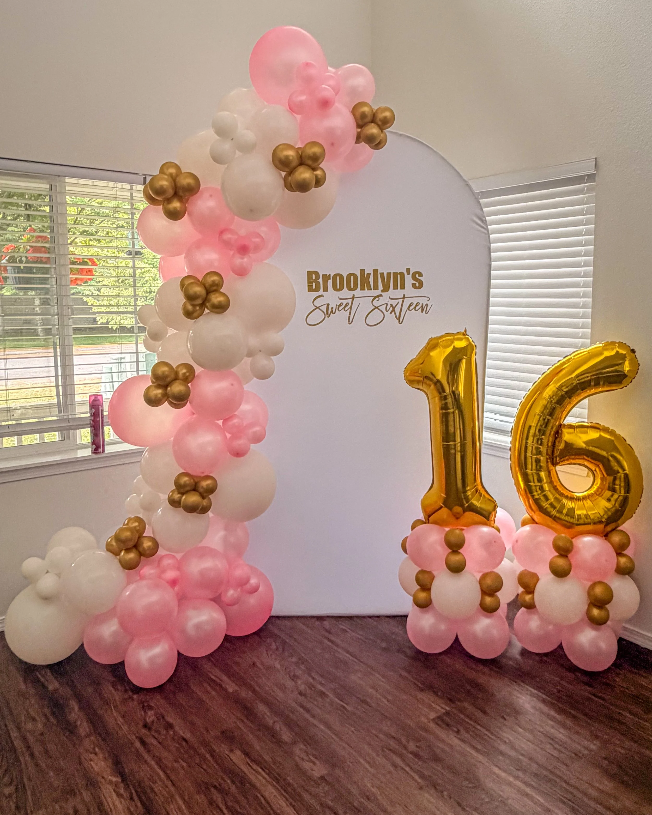 Decorative balloon arrangement for a Sweet Sixteen birthday party with pink, white, and gold balloons, including large gold number '16' balloons.