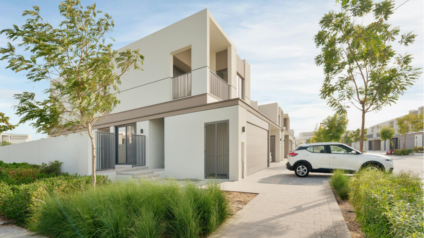Vue d'une maison moderne à deux étages avec un garage, des arbres, un trottoir et une voiture blanche garée devant.