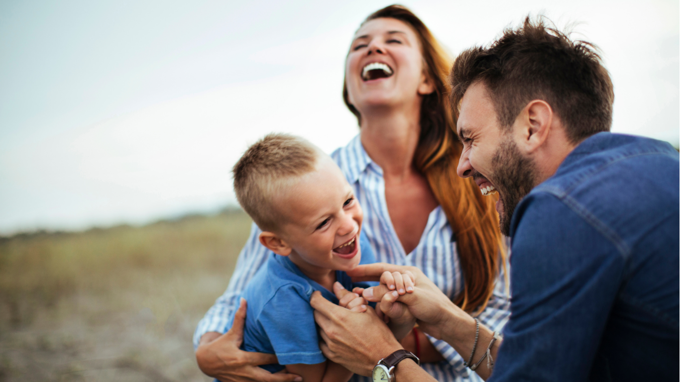 Une famille heureuse souriante joue dehors, un père, une mère et leur fils jeune en pleine rigolade.