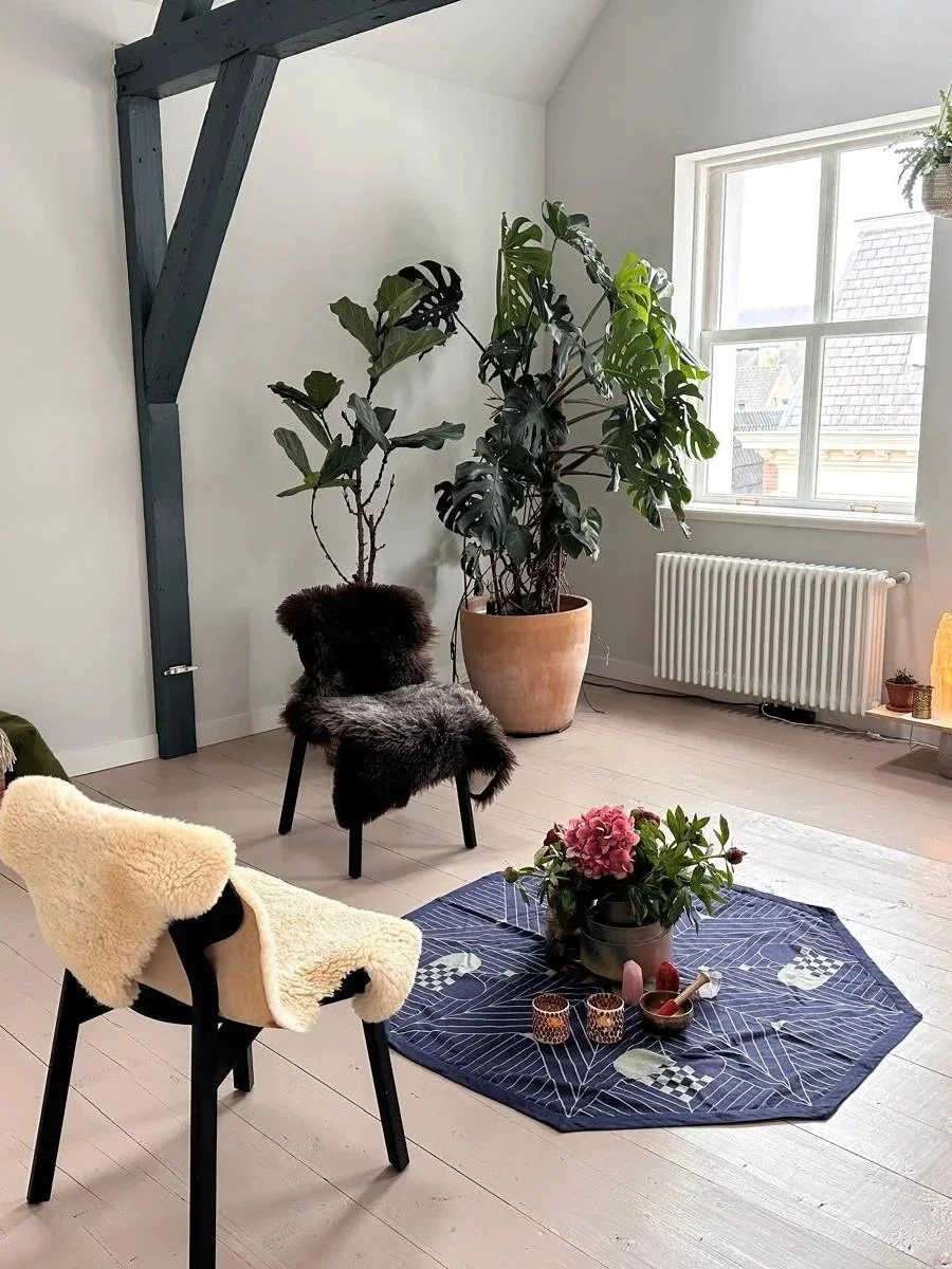Rustige meditatieruimte met stoelen, zachte schapenvachten, planten, bloemen en kaarsen rondom een ceremonieel kleed.