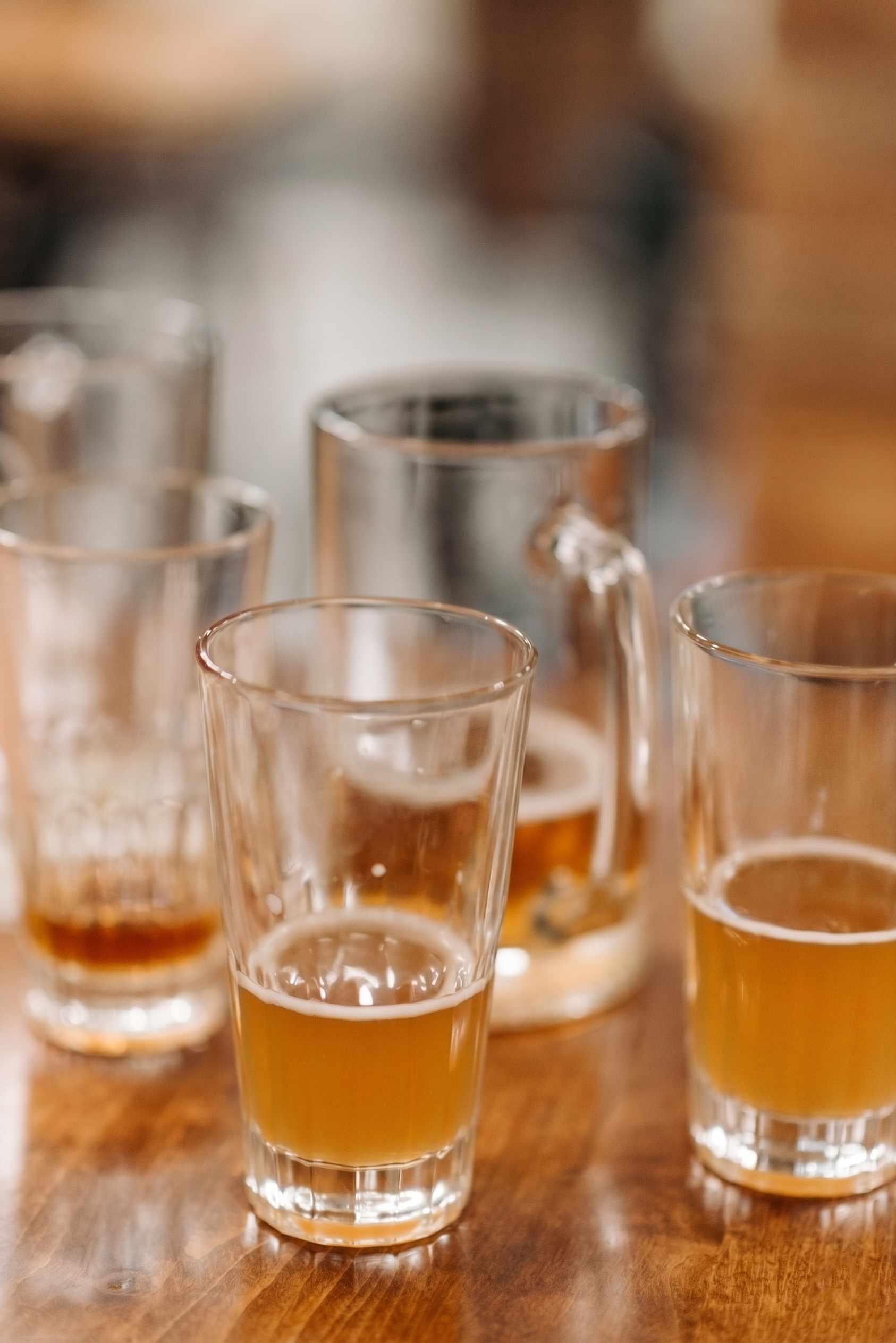 Several shot glasses filled with beer on a wooden table.