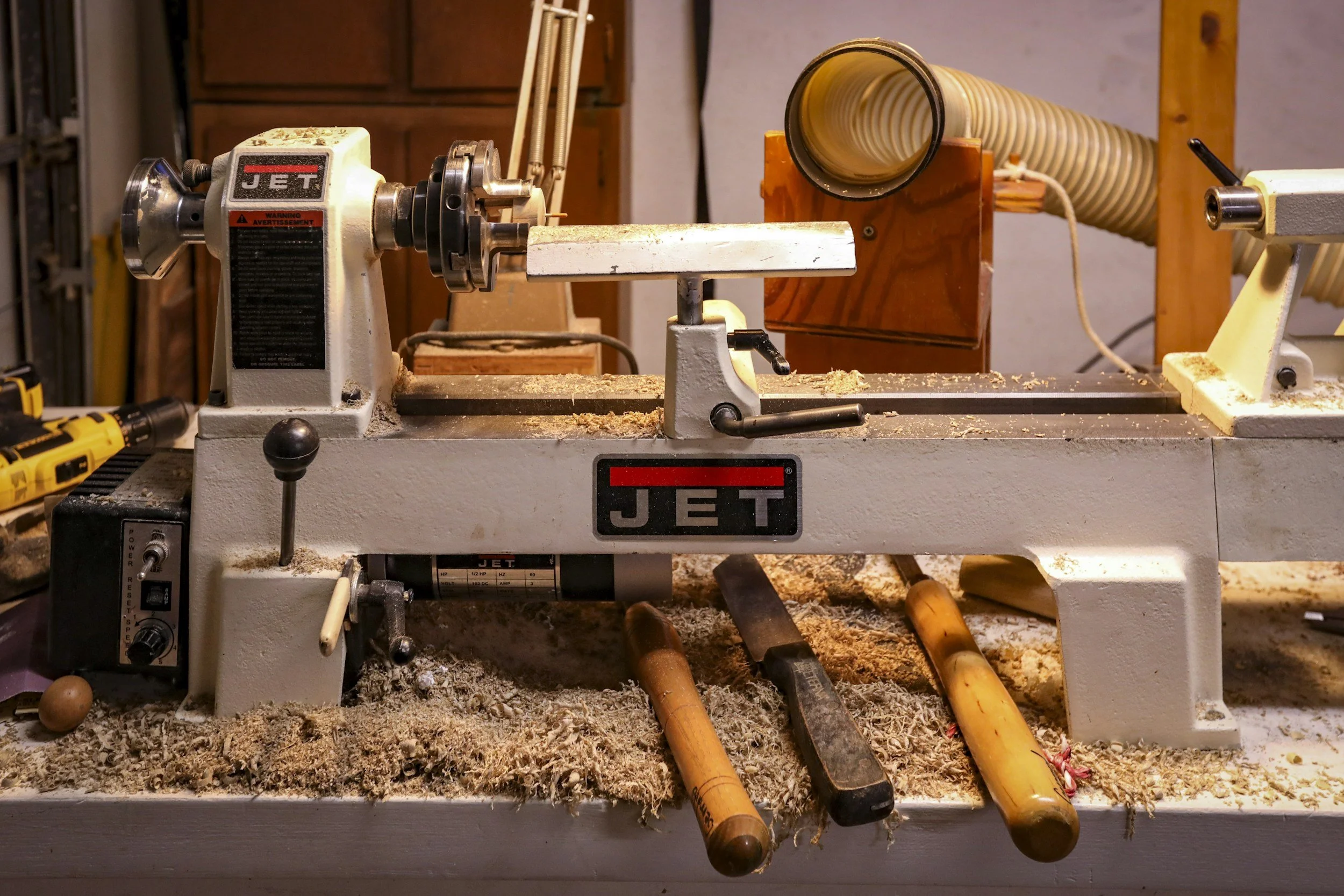 Wood lathe machine in a woodworking shop with tools and wood shavings around it.
