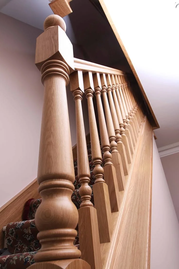 Close-up of a wooden staircase bannister with turned spindles and a newel post, viewed from below.