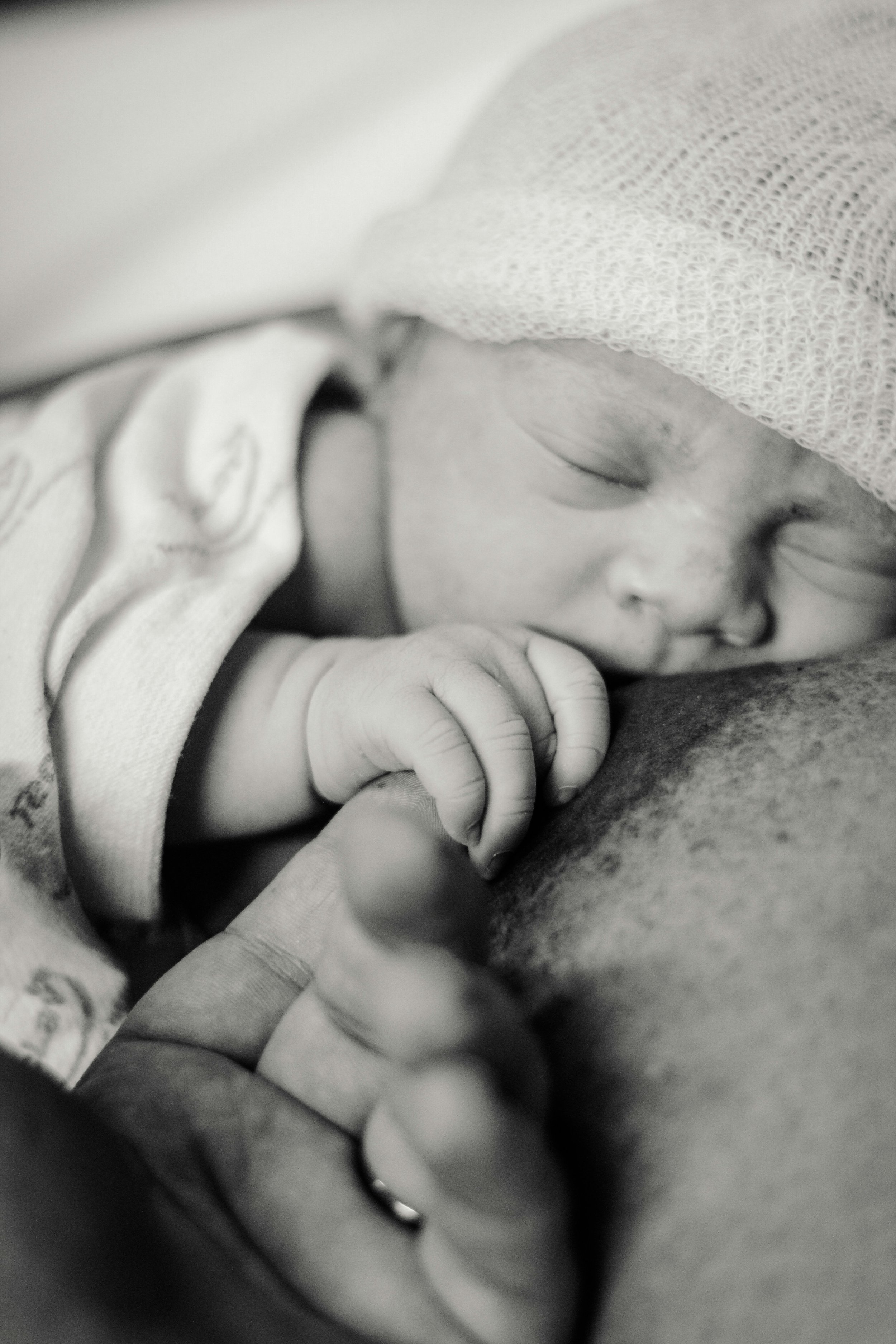 Close-up of a sleeping baby with a blanket covering part of their face, hand near cheek, and tiny fingers curled.
