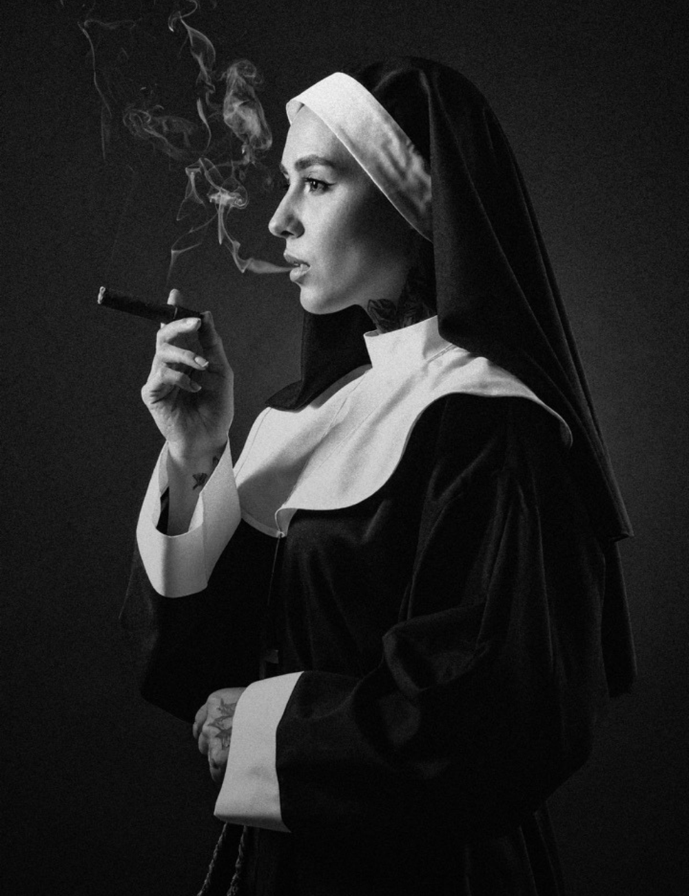 Black and white photo of a woman dressed as a nun smoking a cigarette, with smoke rising and a serious expression.