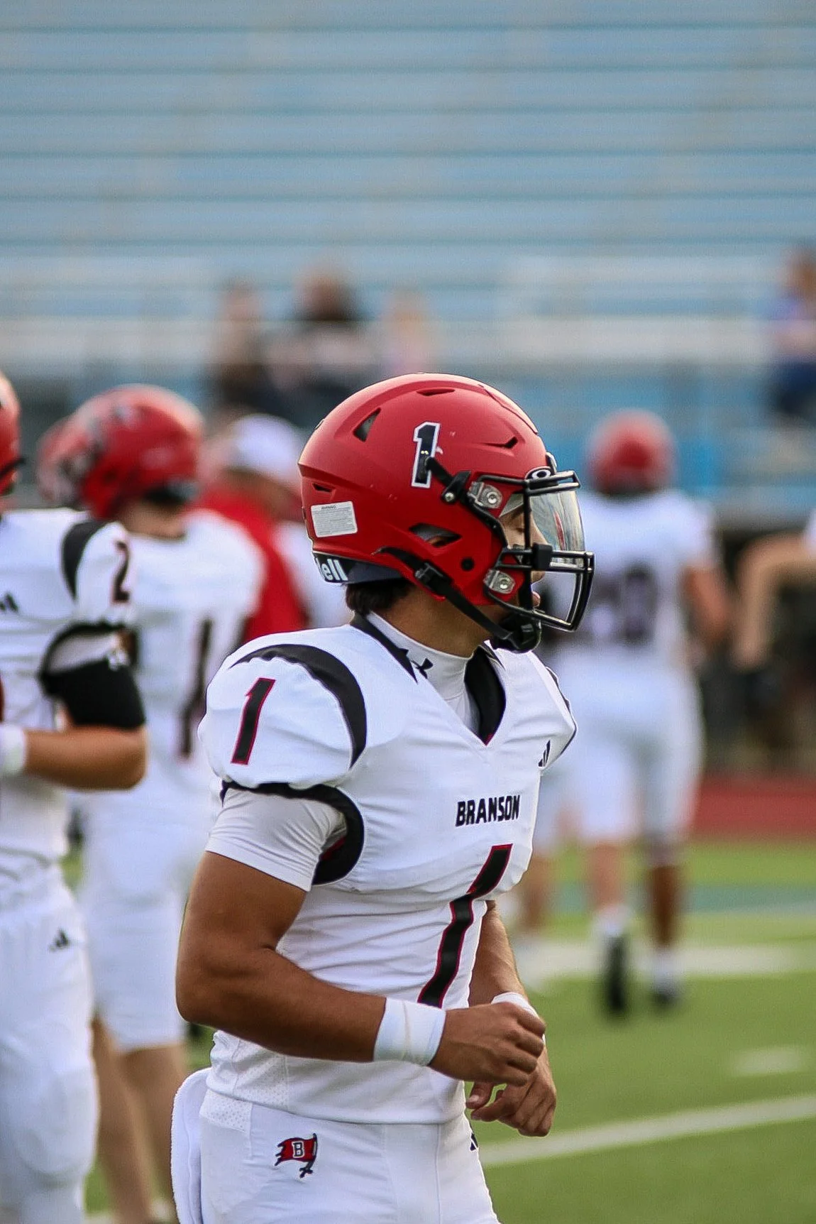 A football player in a white uniform with black and red accents, wearing a red helmet with the number 1, standing on the field during a game.