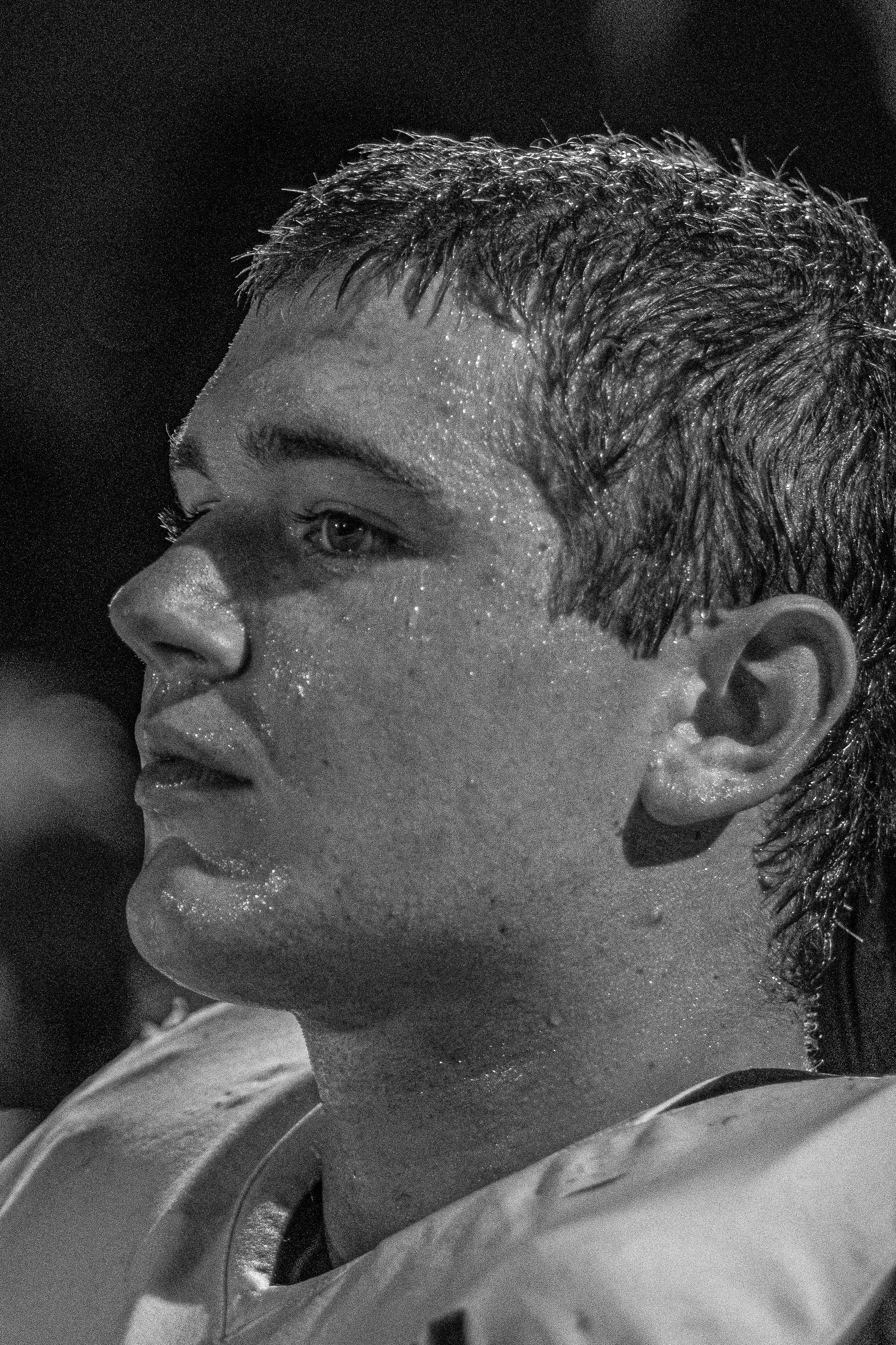 Close-up of a young male athlete with short wet hair, sweat on his face, and a serious expression, captured in profile.