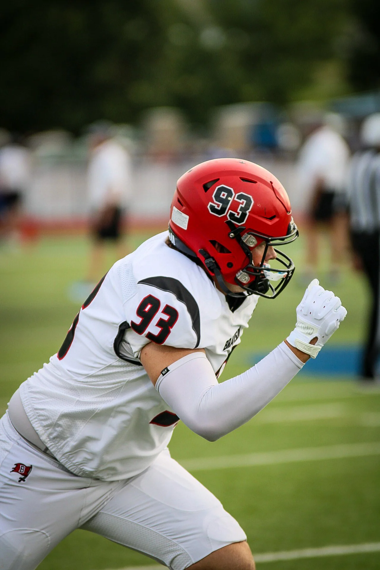 A football player wearing a red helmet with the number 93, white and black uniform, in a running stance on the field.