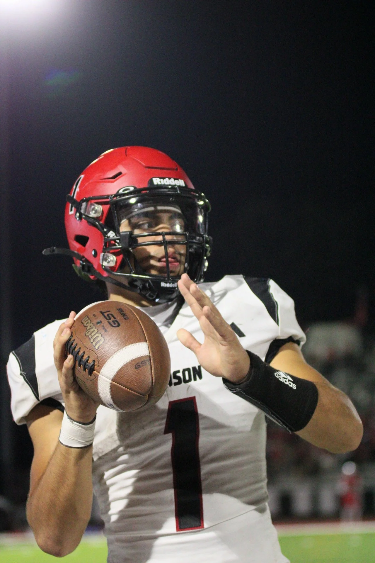 A football player in a white jersey and red helmet holding a football during a game at night.