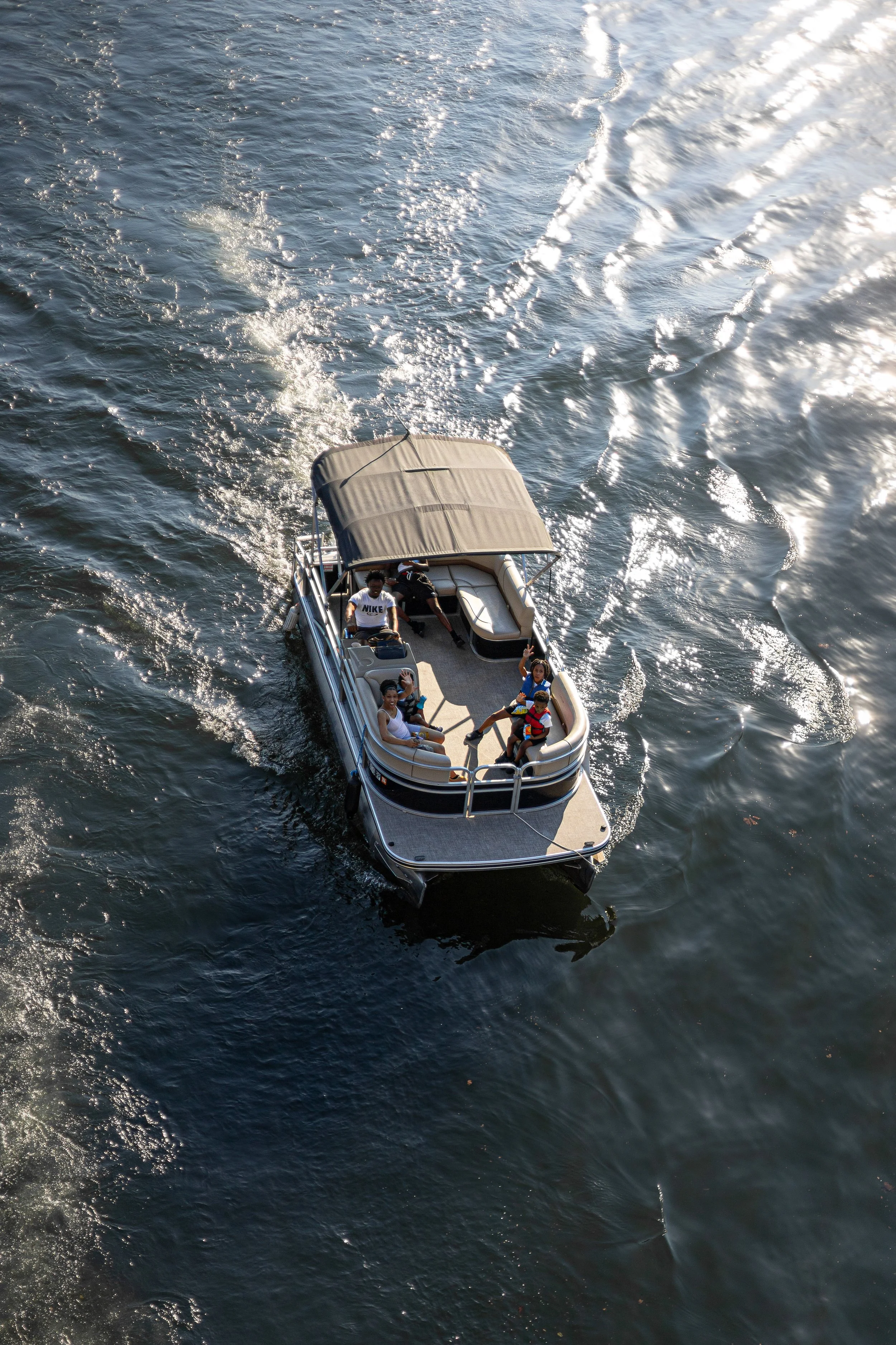 A boat with five people on a body of water during daytime, some of them are waving.