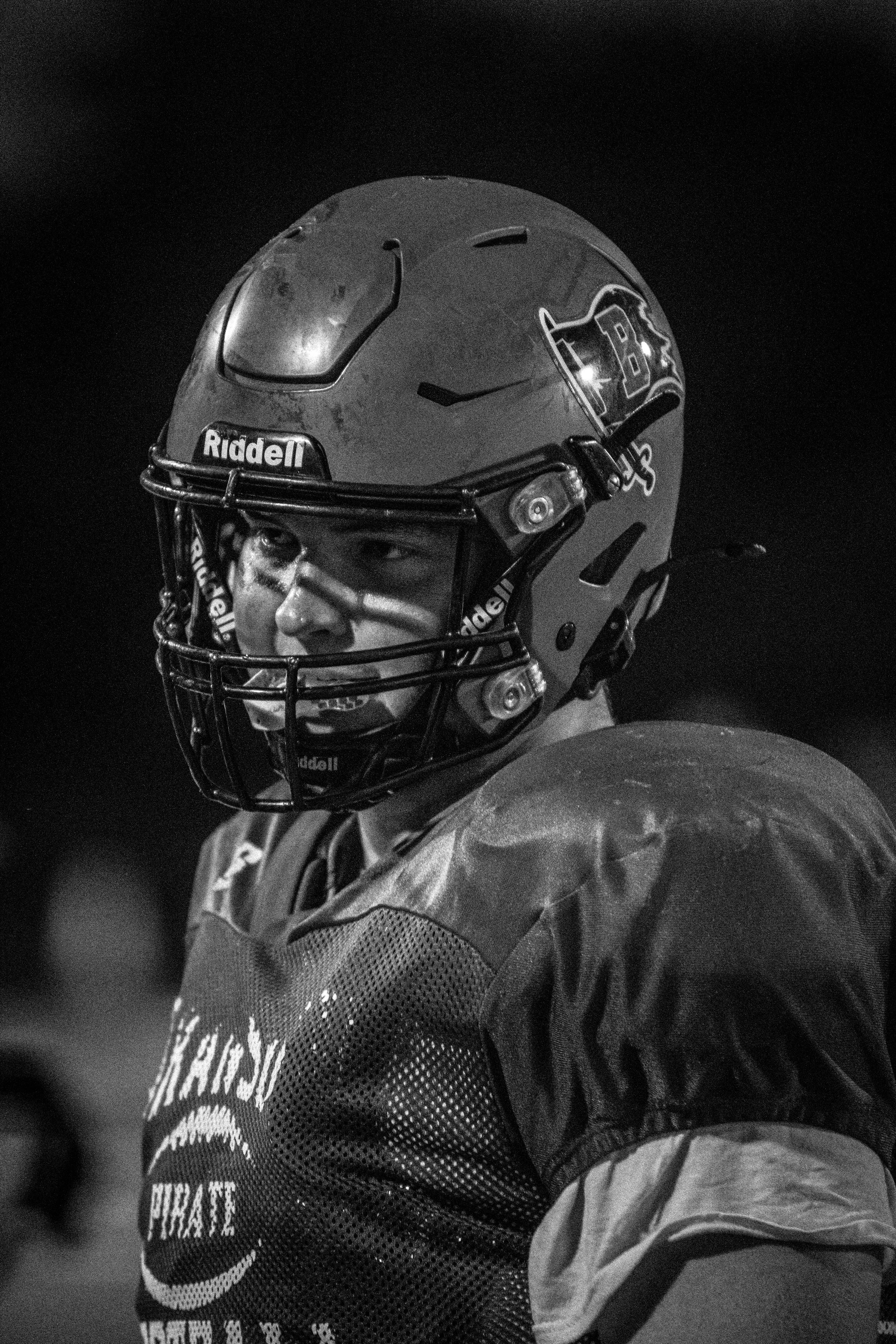 A football player wearing a helmet with a faceguard, looking to the left, in a team uniform. Black and white photo.