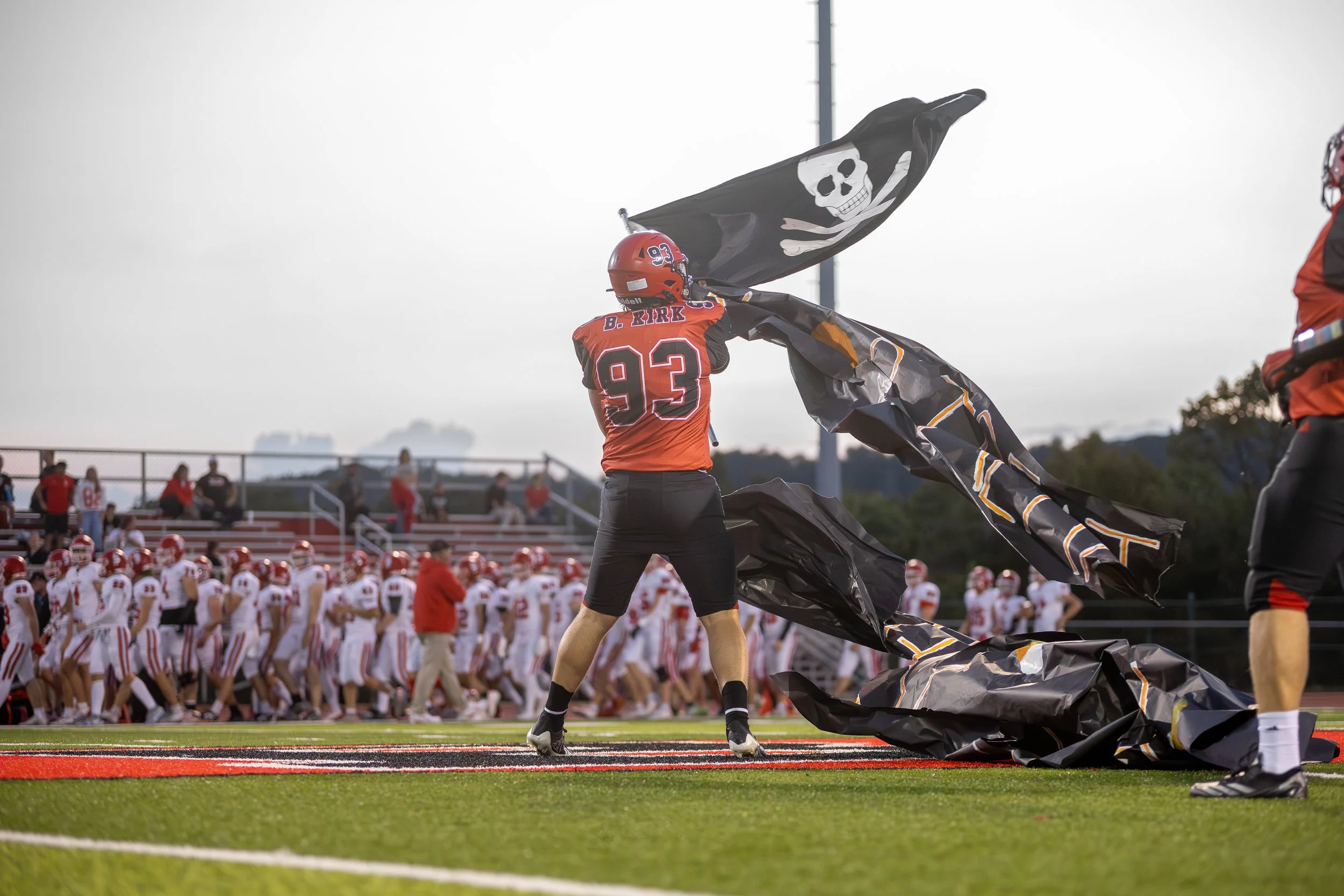 Football player with the number 93 on his uniform removing a black pirate flag with a skull and crossbones from the sideline during a game.