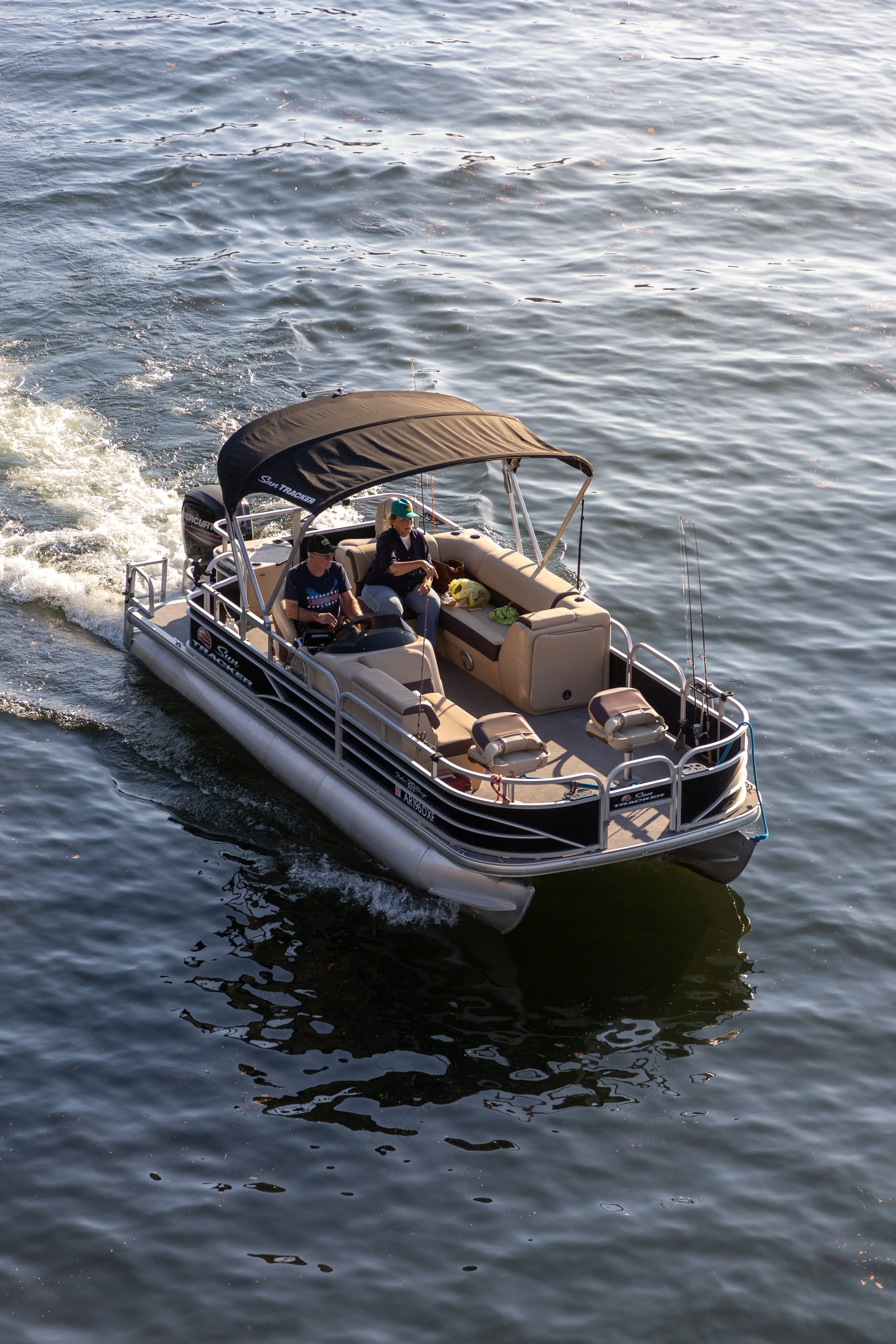A pontoon boat with two people on board, out on the water, with a canopy and fishing rods.