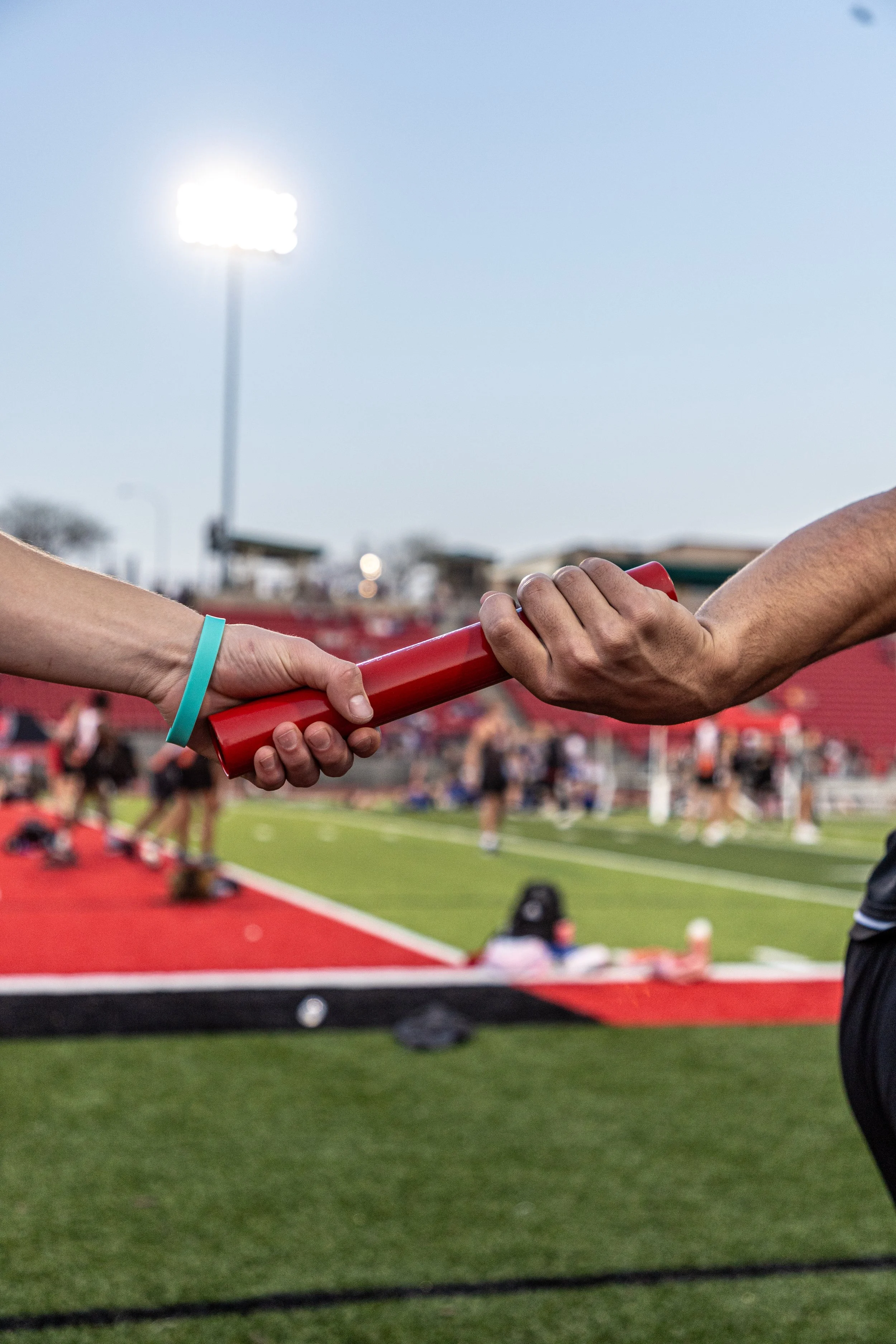 Two people passing a baton during a relay race at a track and field stadium.