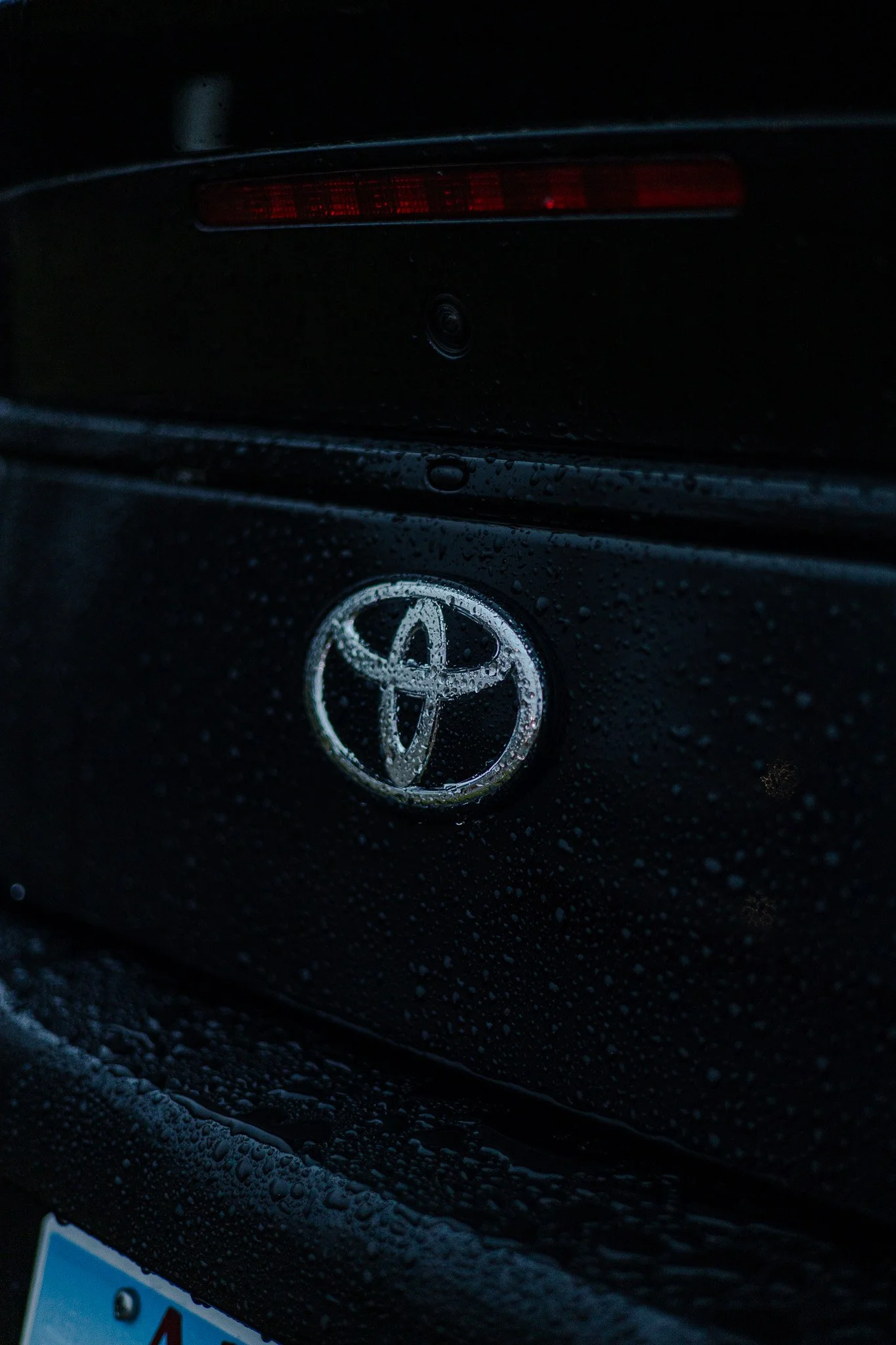 Close-up of the rear of a black Toyota car, showing water droplets on the surface, with the Toyota logo prominently in the center.
