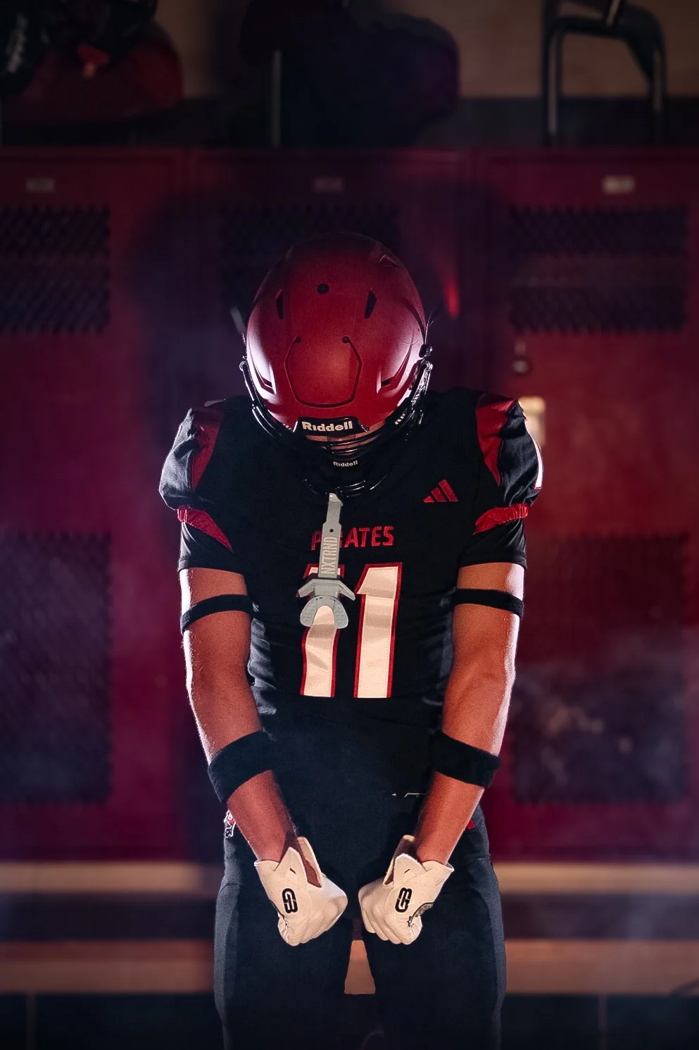 A football player in a red helmet and black jersey with red accents, number 11, standing in a locker room.