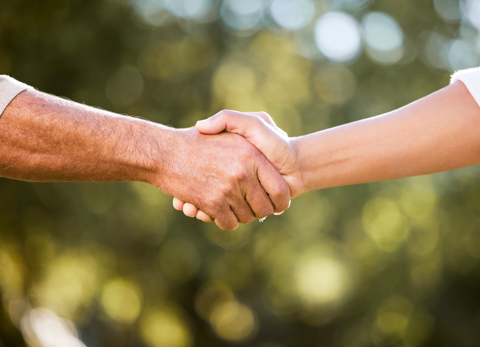 Close-up of two people shaking hands outdoors, illustrating the importance of friendship and connection for men.