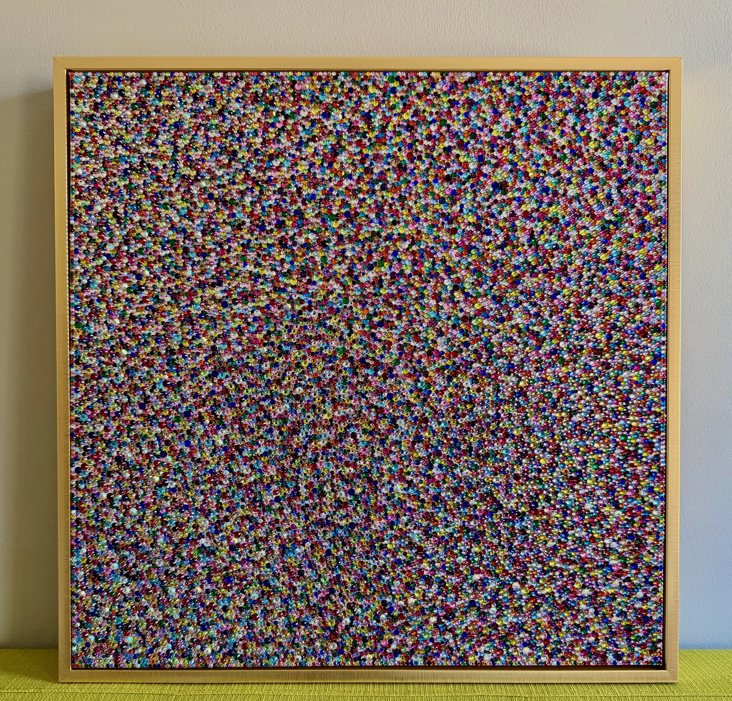 Panic (2026), 20x20 in. Multicolored sculptural panel in a gold frame, displayed on a yellow couch to show scale and prismatic texture.